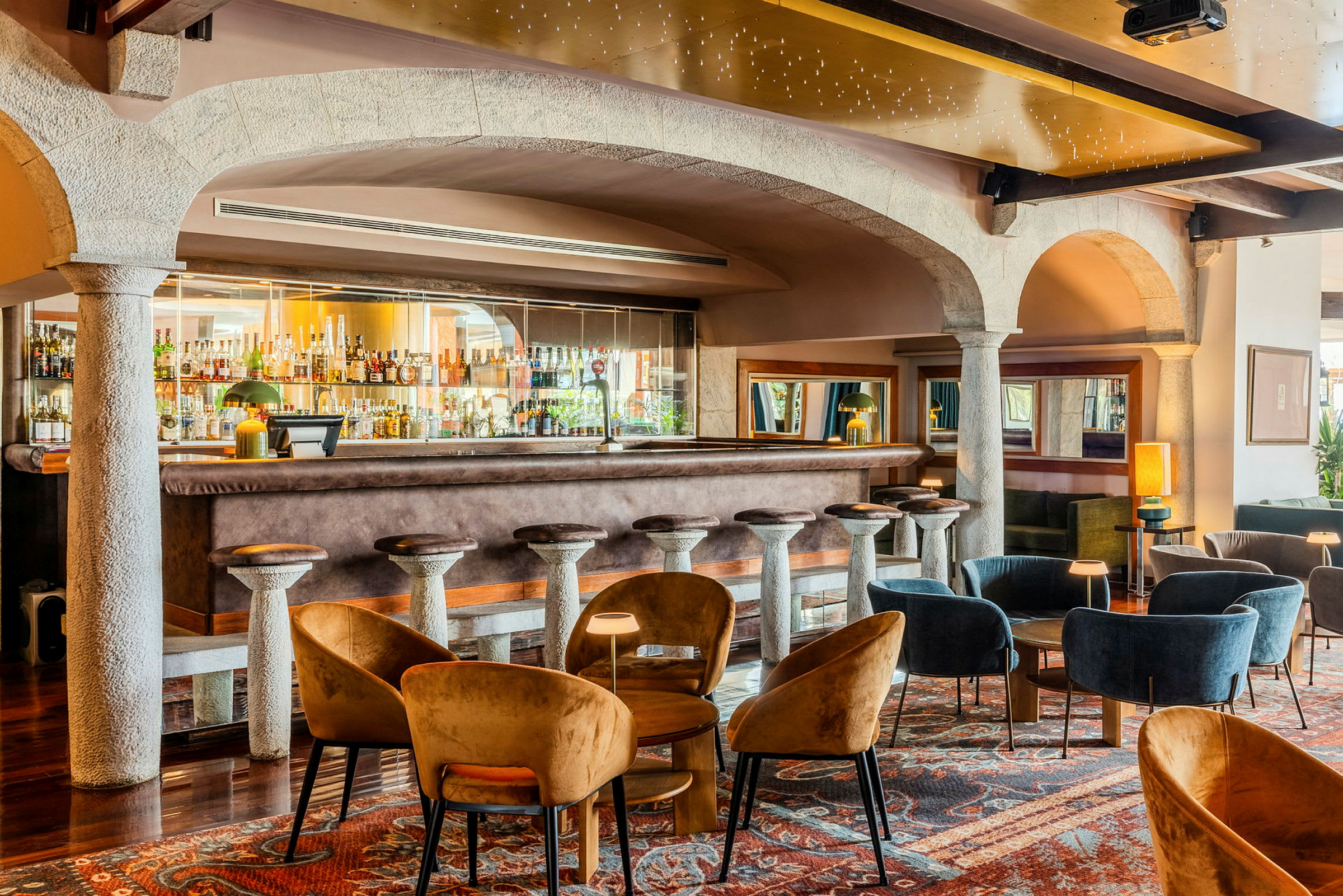 Bild av en elegant bar med en bardisk omgiven av höga barstolar samt sittplatser med soffor och stolar i ett stilfullt inrett område. (AI-genererad text)