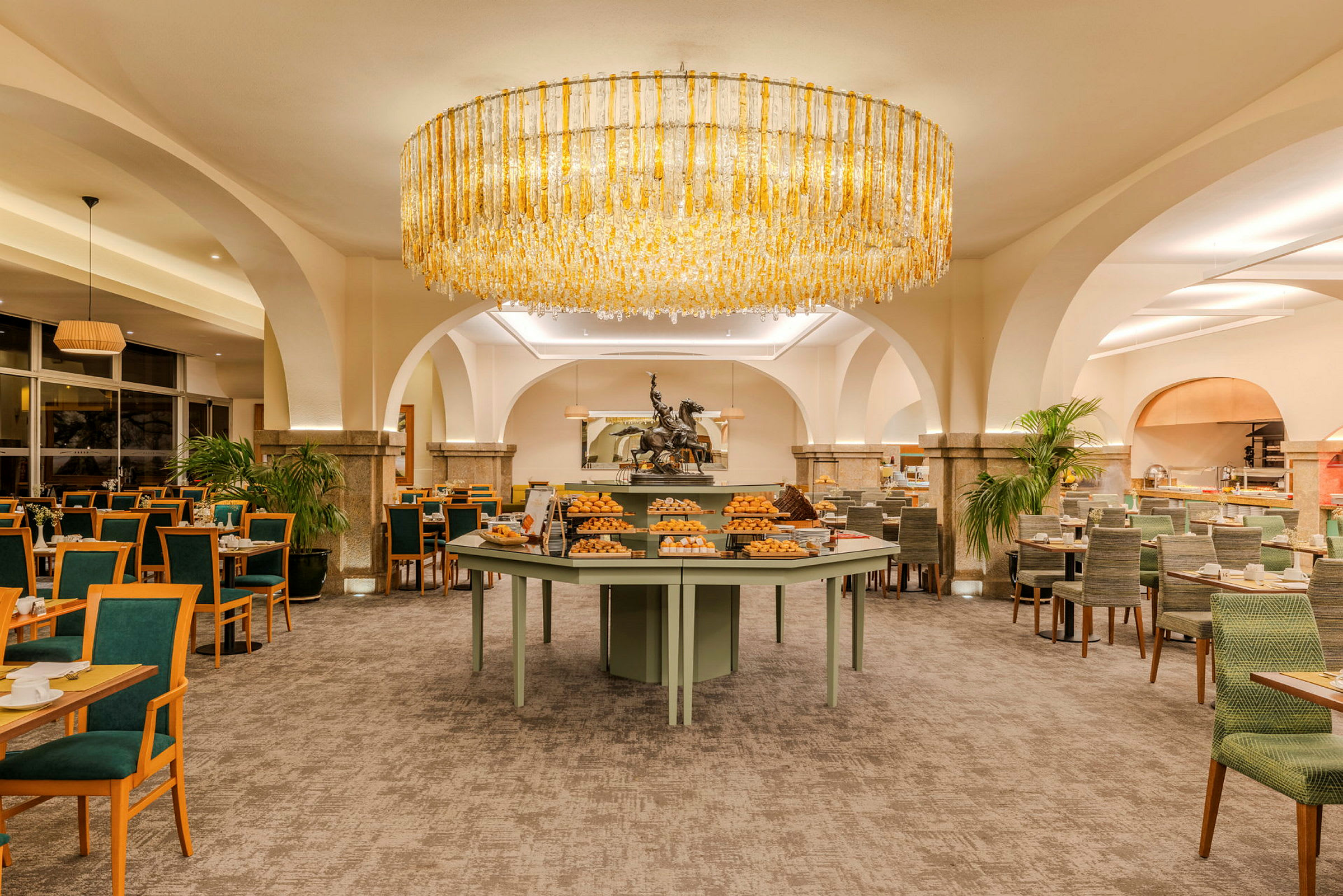 Ett välbelyst hotellrestaurang med ett runt bord fullt av bröd och bakverk i mitten. (AI-genererad text)