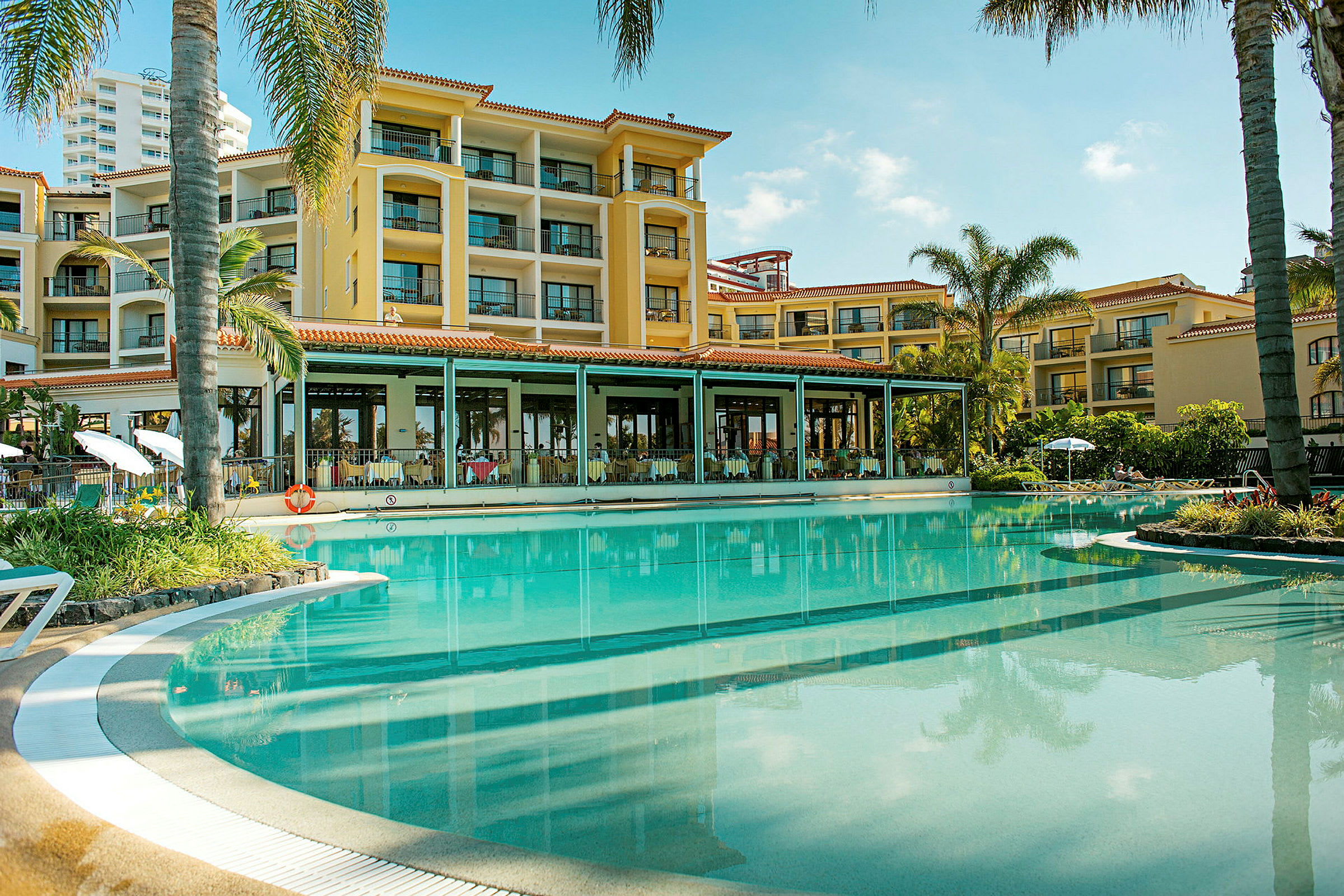 Hotellbyggnad nära en pool med omgivande palmer. (AI-genererad text)