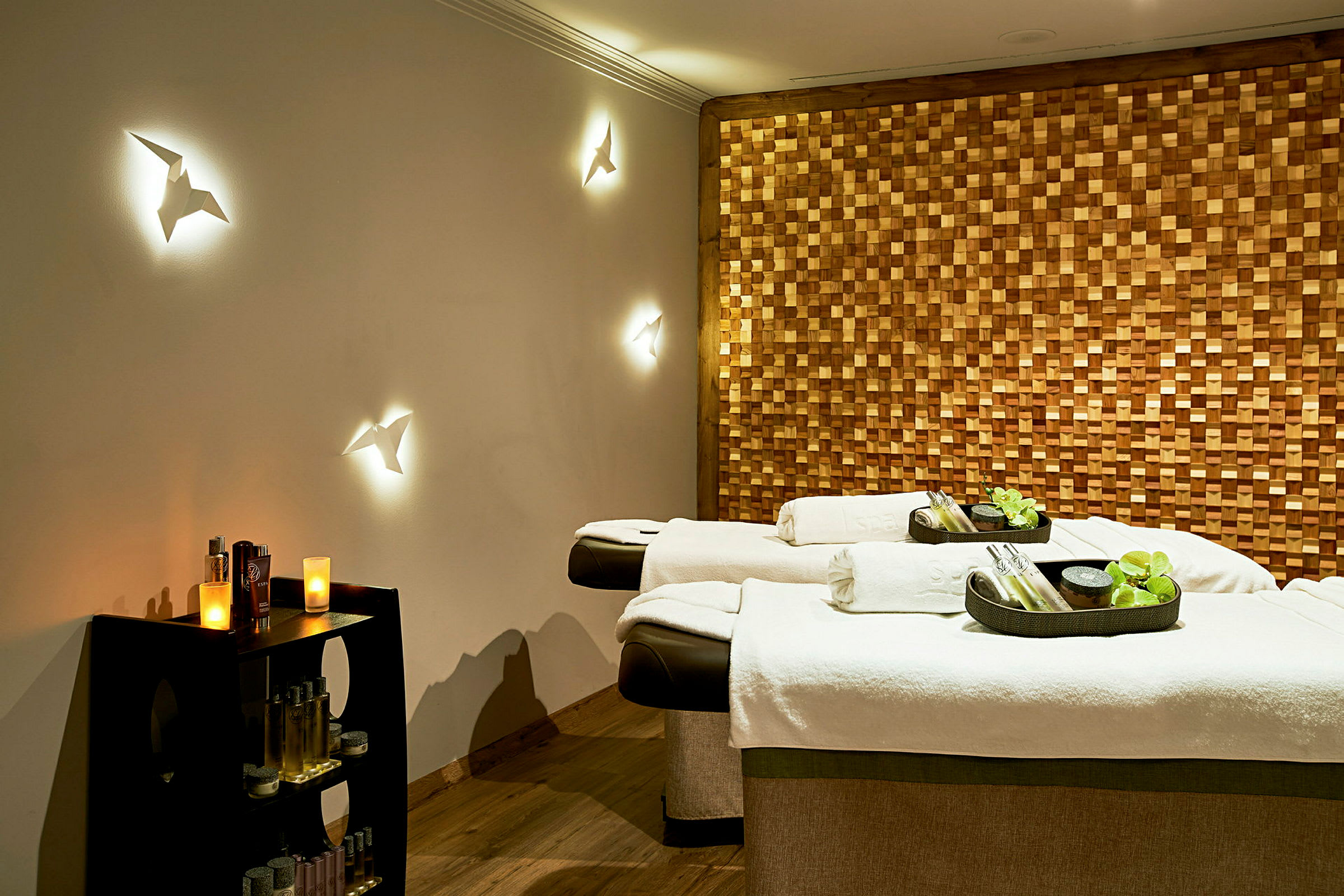 Ett spa-rum med två massagebänkar, dekorativa vägglampor och en trävägg. (AI-genererad text)