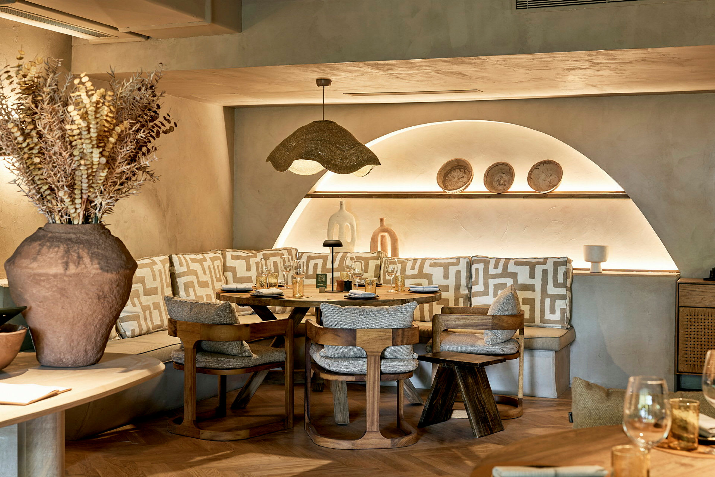 Ett stilfullt restaurangbord omgiven av stolar och bänkar med geometriska mönstrade kuddar. (AI-genererad text)