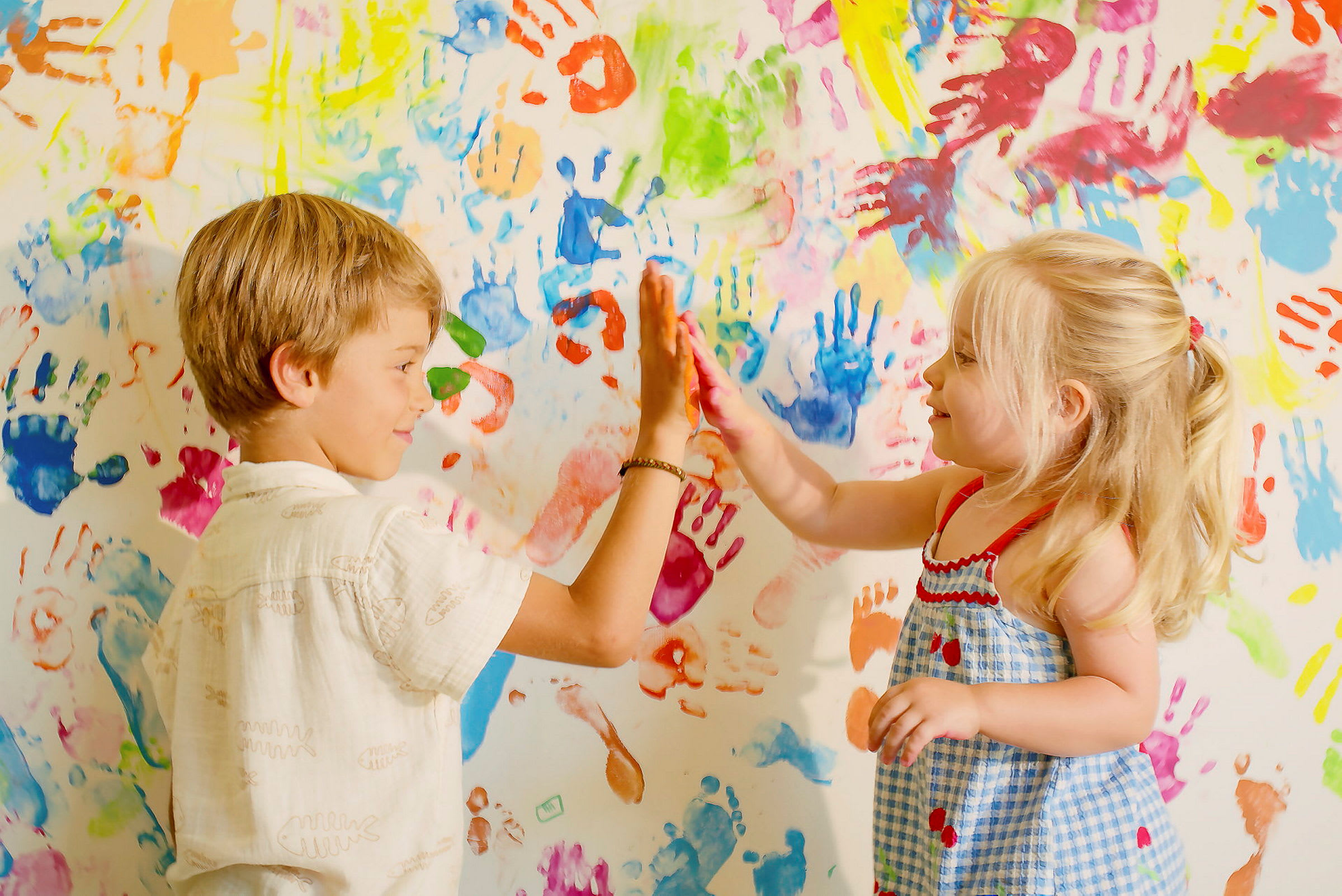 Ett barn och en flicka gör en high-five framför en vägg med färgglada handavtryck. (AI-genererad text)