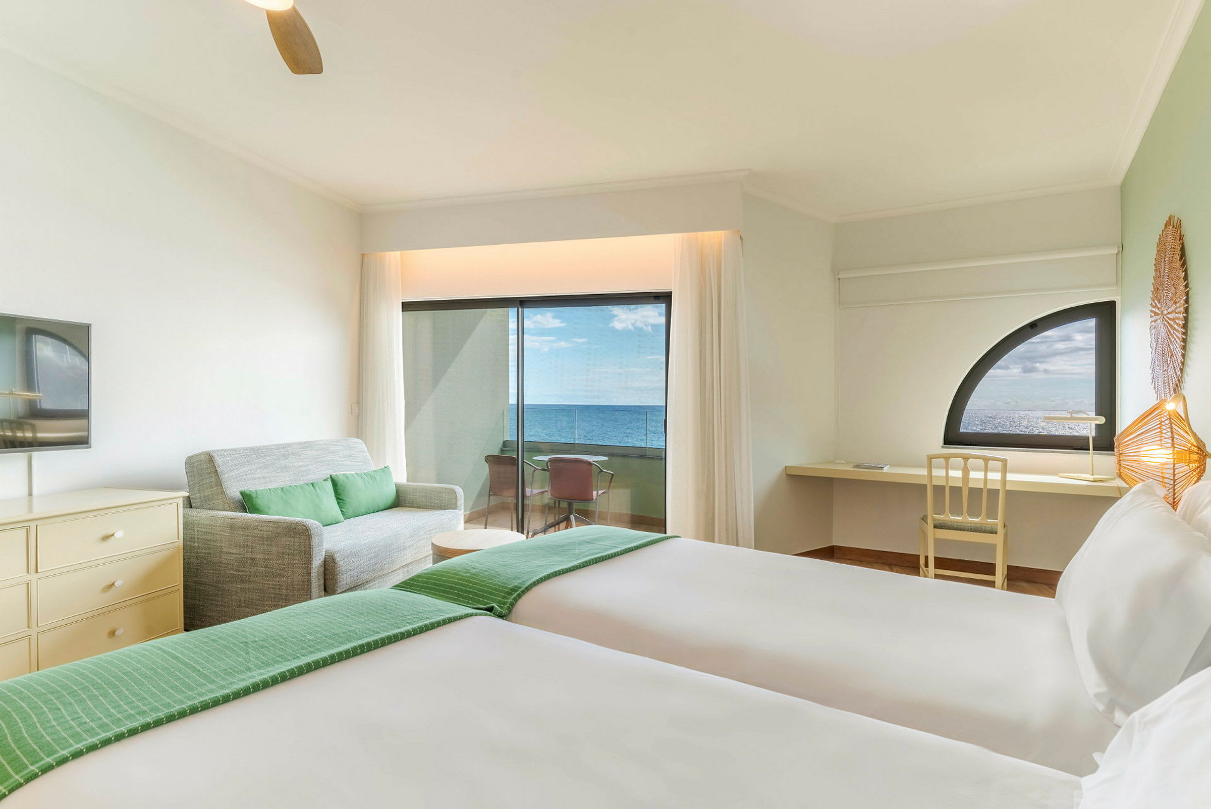 Hotelrum med två sängar, en soffa, ett skrivbord och en balkong med havsutsikt. (AI-genererad text)