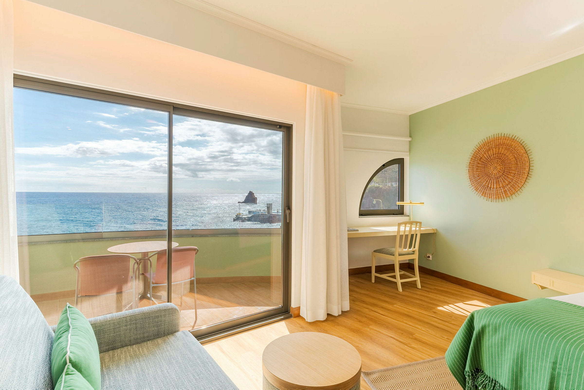 Ett hotellrum med utsikt över havet genom stora glasdörrar. På verandan finns en sittgrupp och interiören är ljus och modern. (AI-genererad text)