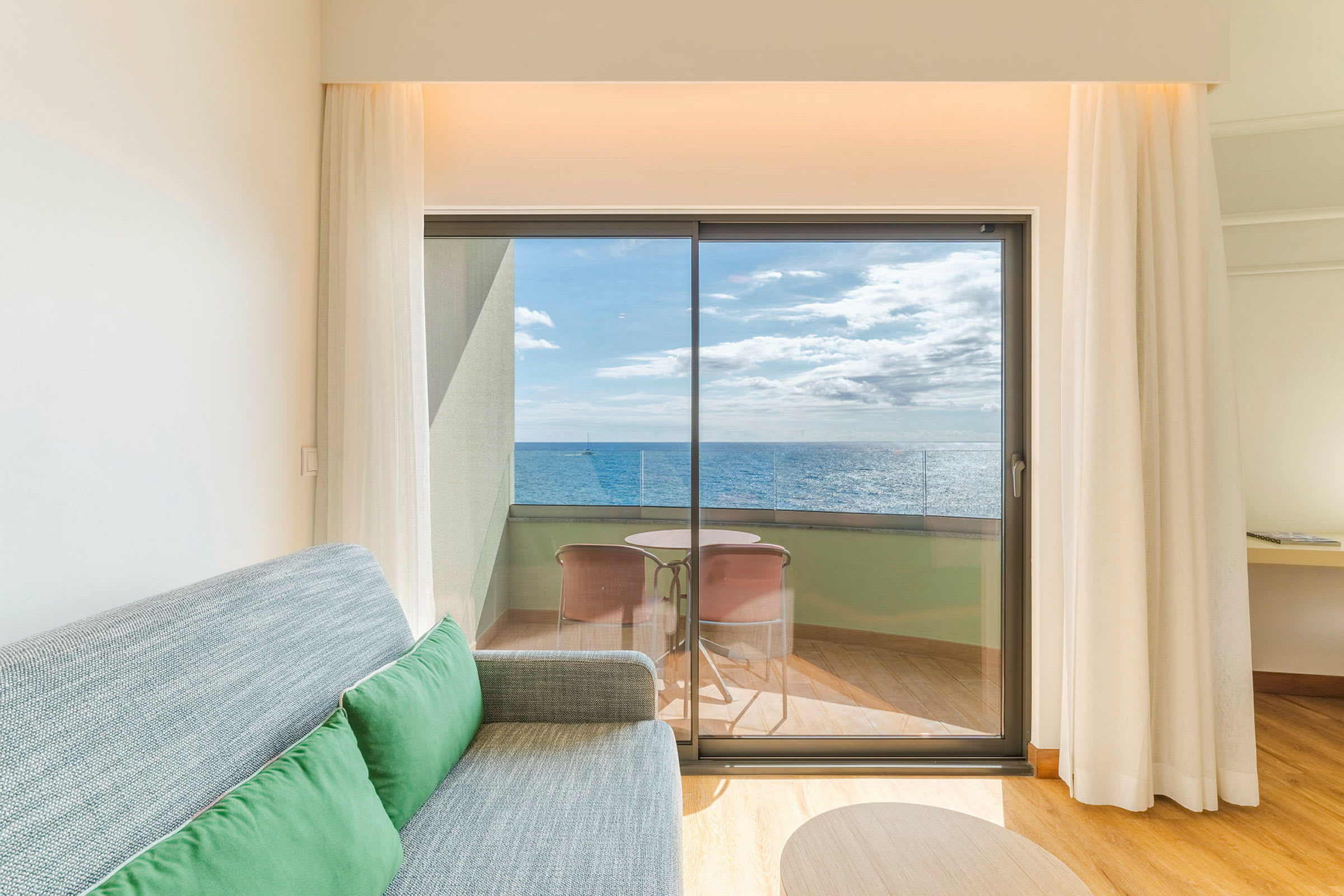 Ett hotellrum med en soffa och utsikt mot en balkong med havet i bakgrunden. (AI-genererad text)