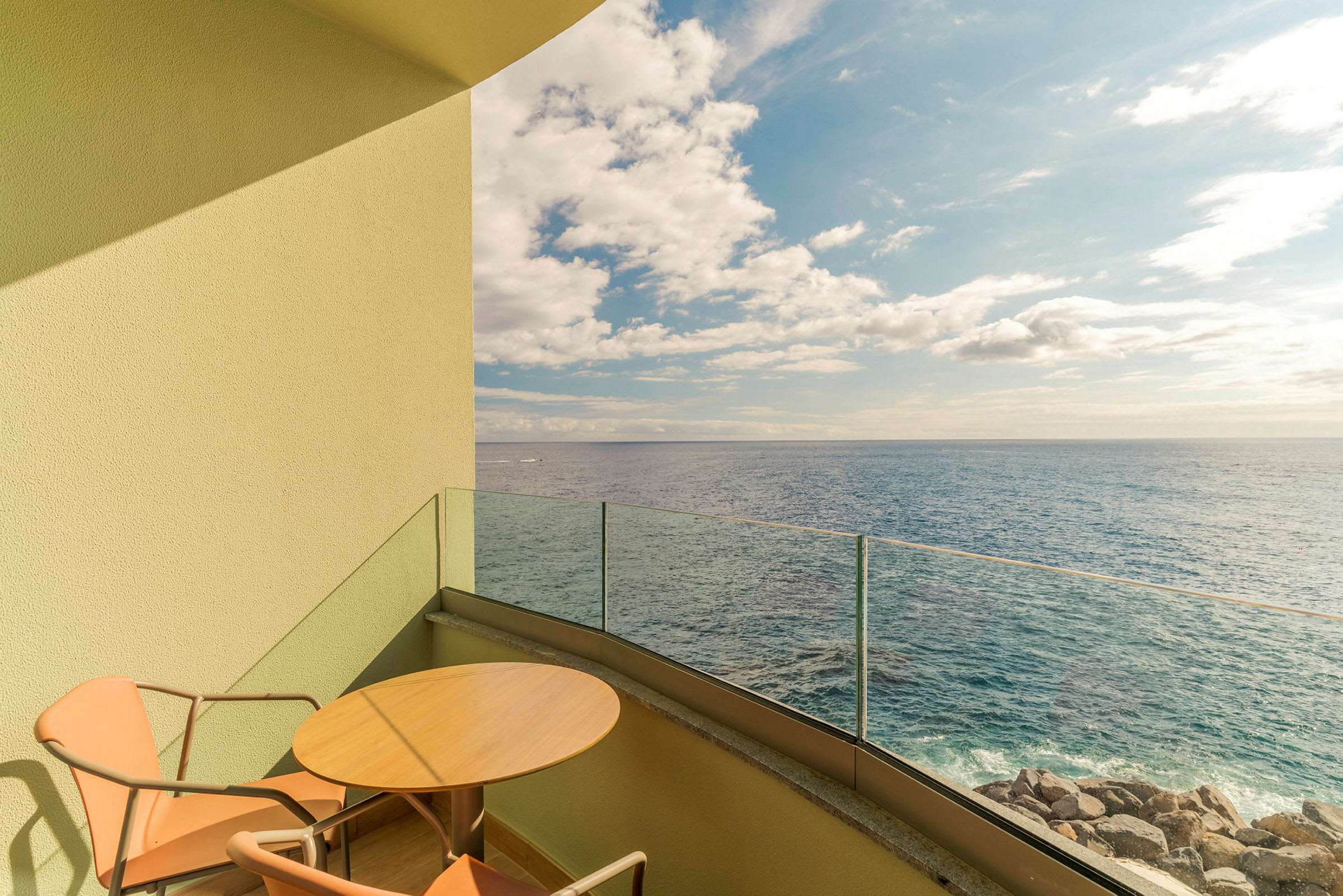 En balkong med ett bord och två stolar som vetter mot havet under en klar himmel. (AI-genererad text)