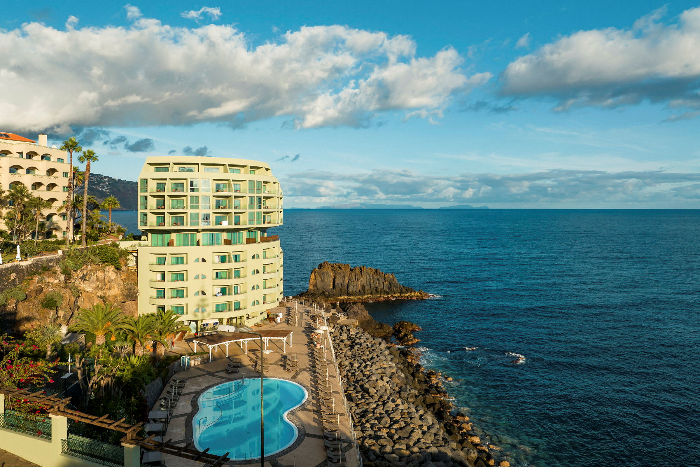Ett hotell med pool ligger vid havet och omringas av klippor och växtlighet. (AI-genererad text)
