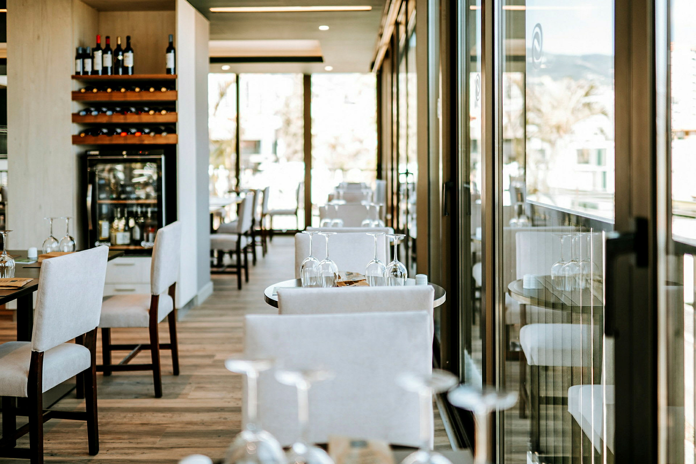 En restaurang med bord och stolar samt glasdörrar som släpper in naturligt ljus. (AI-genererad text)