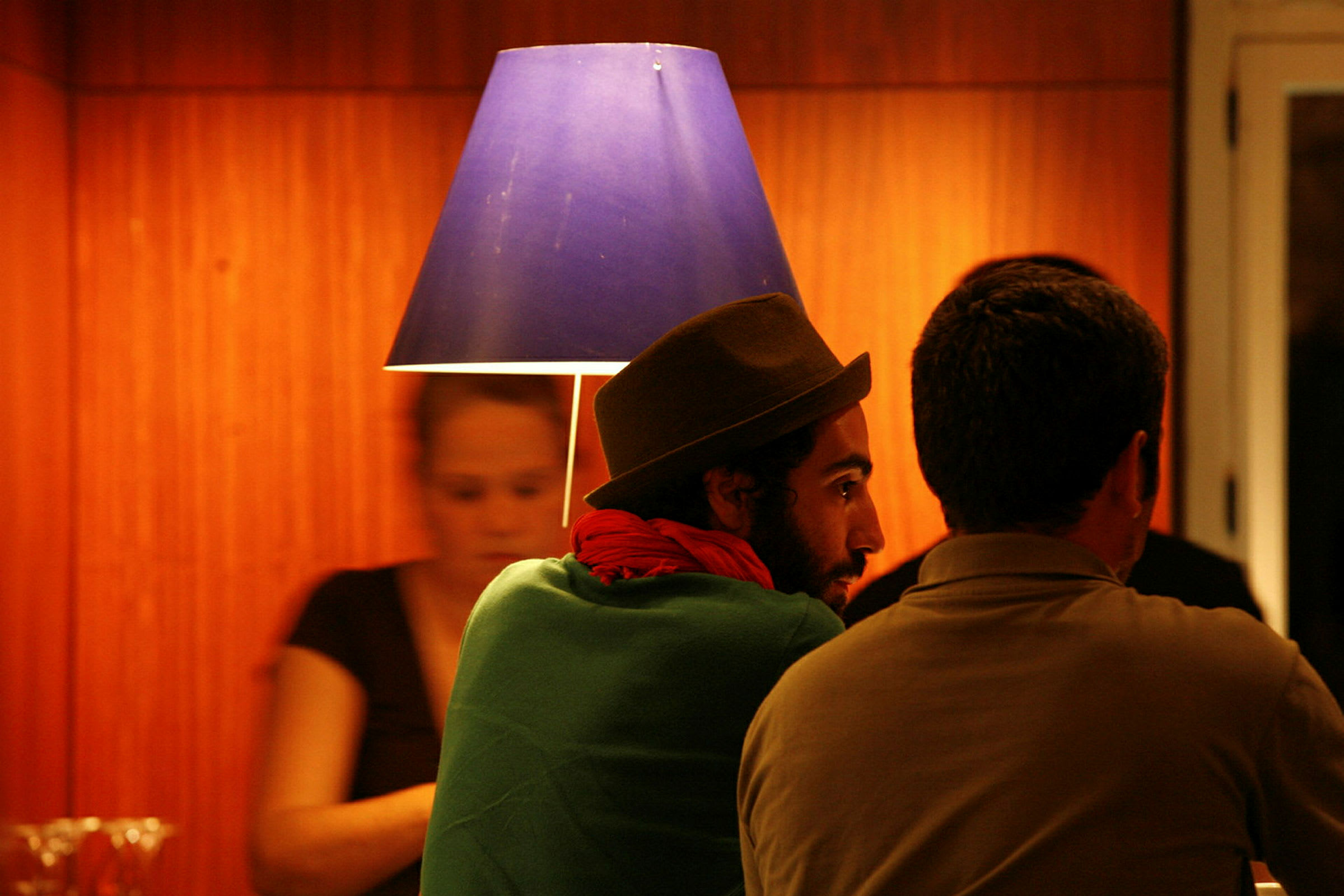Folk sitter vid en bardisk under en blå lampskärm. (AI-genererad text)