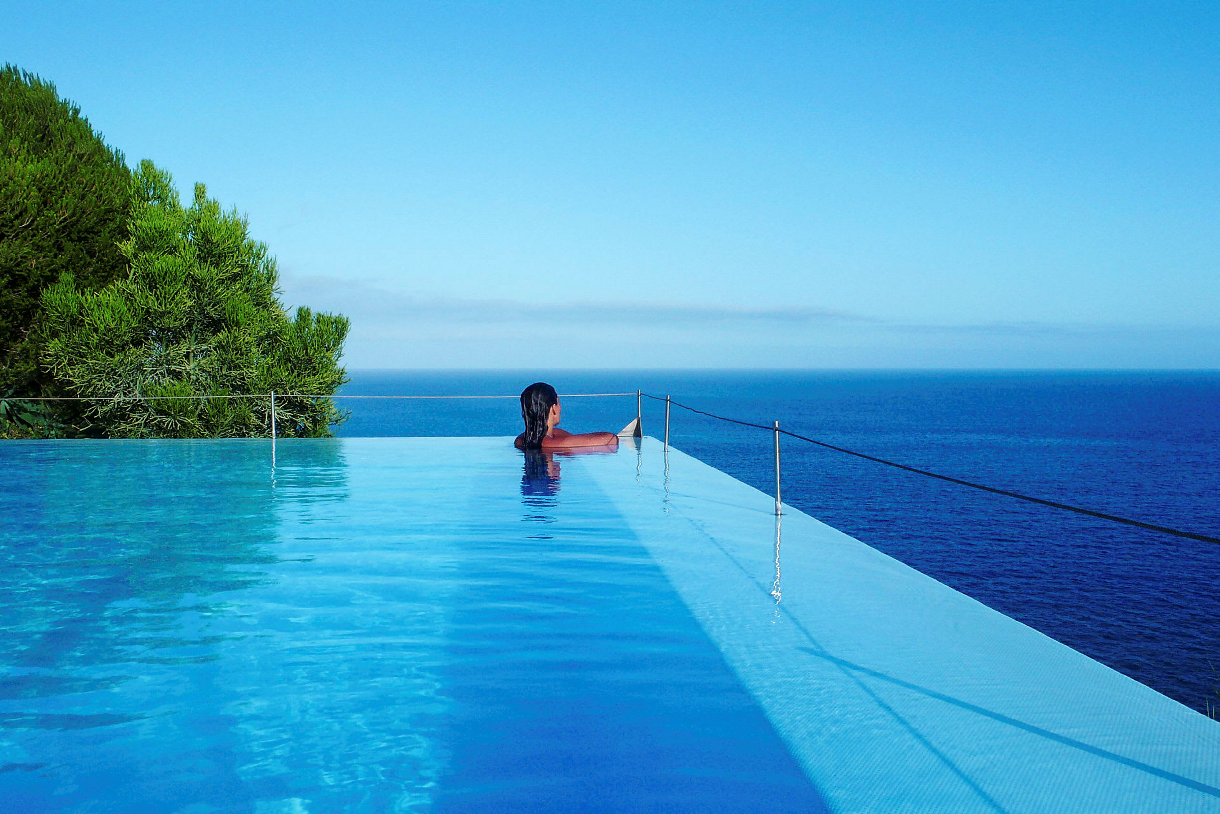 En person sitter vid kanten av en infinitypool med utsikt över havet. (AI-genererad text)
