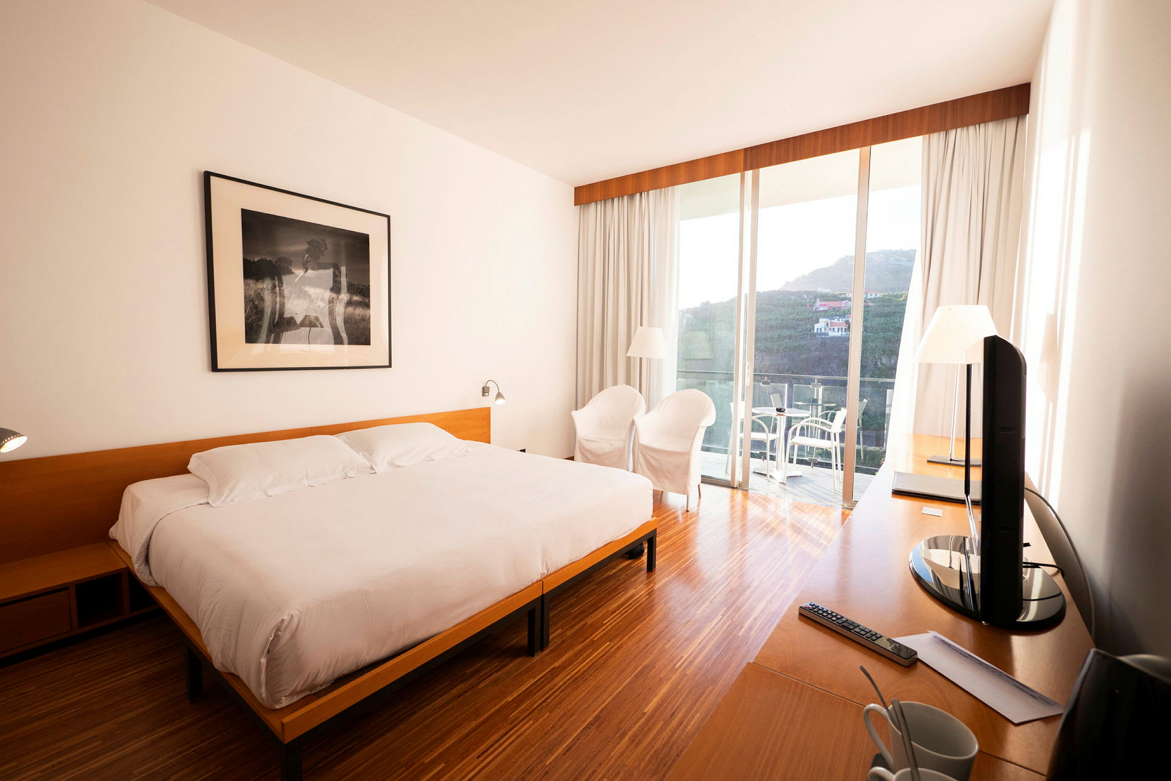 Ett hotellrum med en dubbelsäng, ett skrivbord, två stolar och en terrass med utsikt. (AI-genererad text)