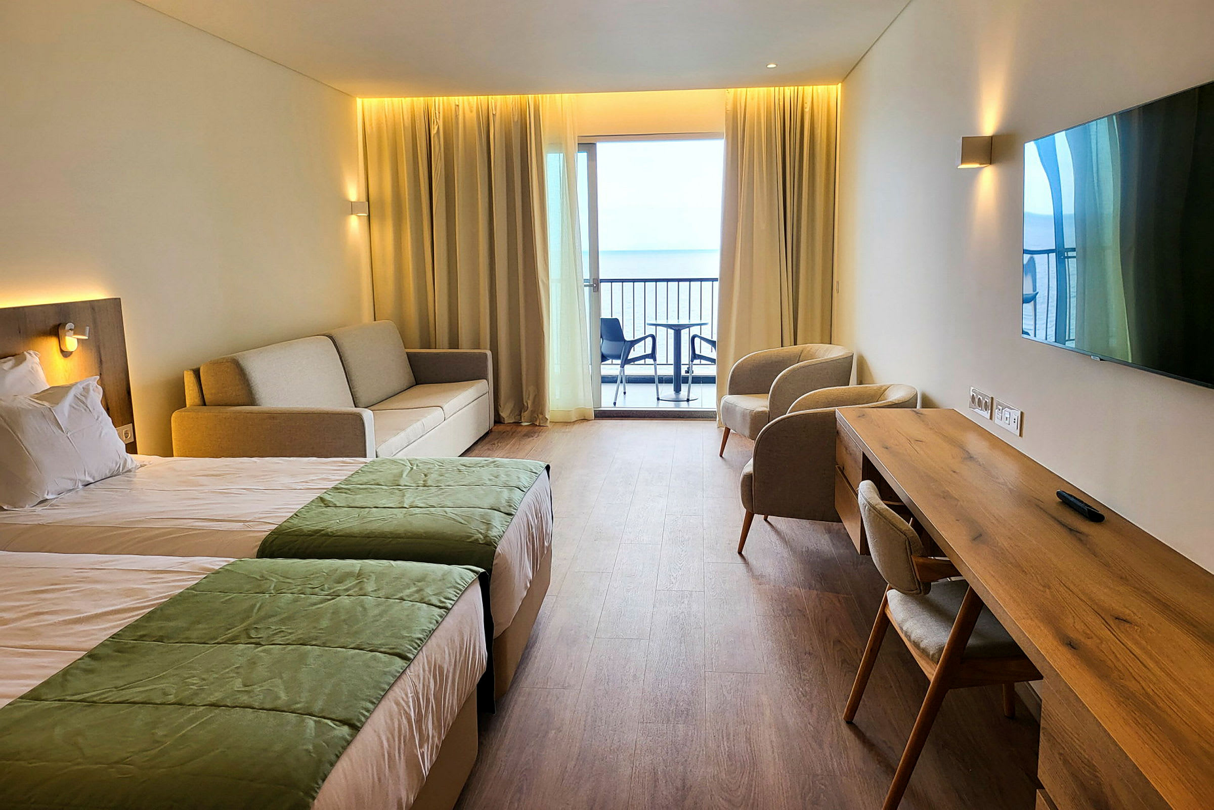 Ett hotellrum med två sängar, soffa, två fåtöljer, skrivbord och en balkong med utsikt. (AI-genererad text)