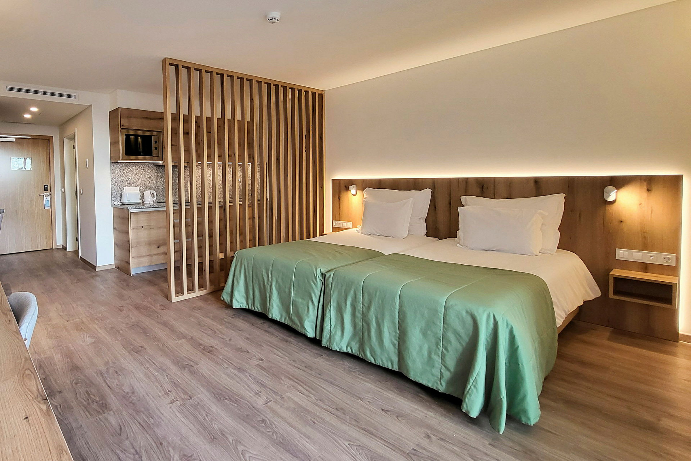 Ett modernt hotellrum med två enkelsängar bredvid varandra, en träpanelvägg och ett litet pentry. (AI-genererad text)
