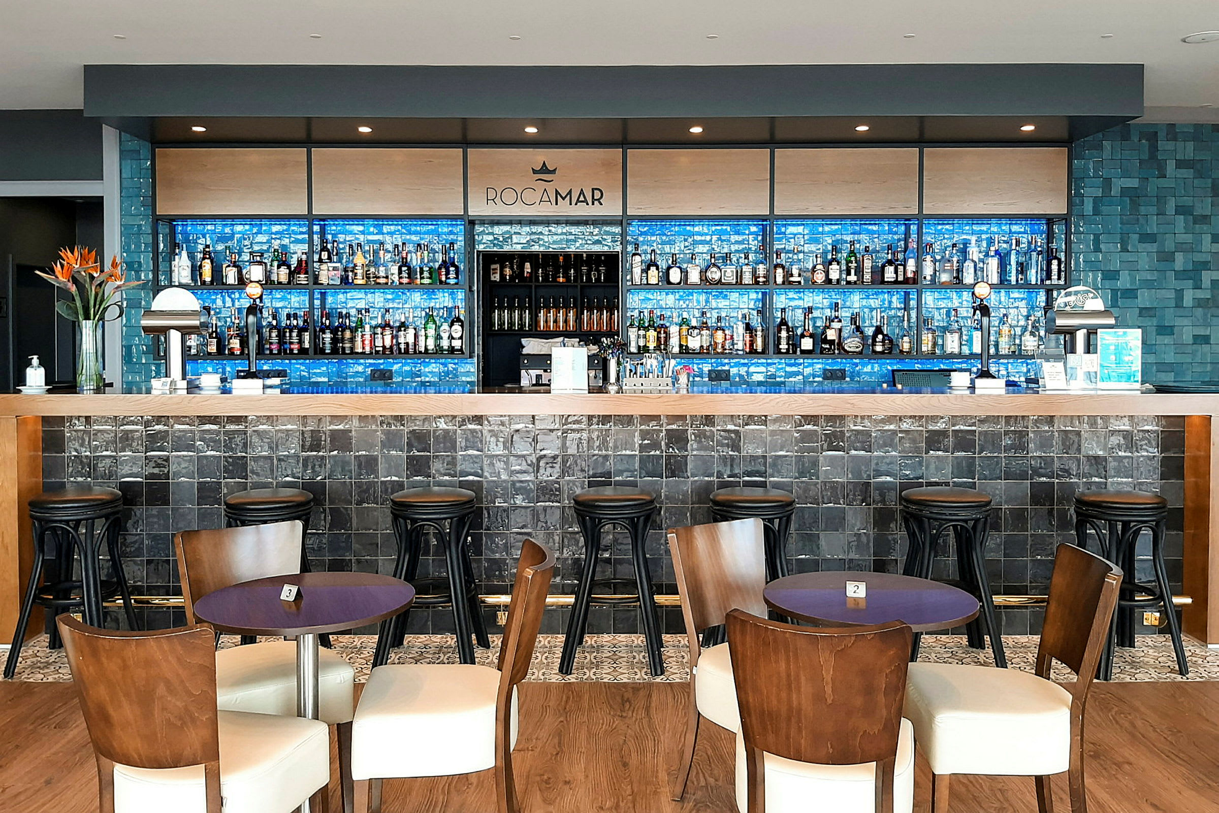 En hotellbar med träbord och stolar framför en lång bardisk. (AI-genererad text)