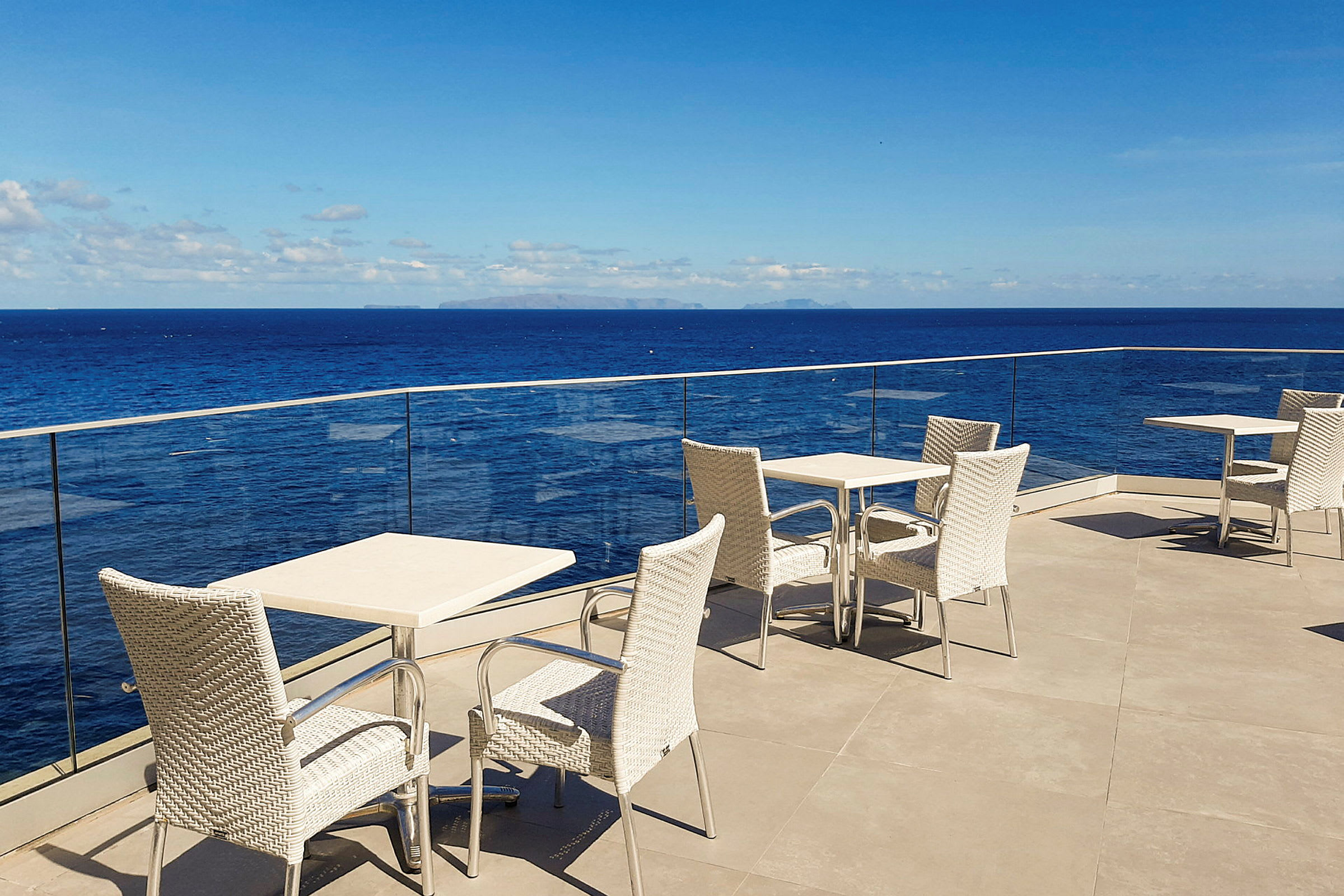 Bords- och stolemöbler på en terrass med utsikt över havet och blå himmel. (AI-genererad text)