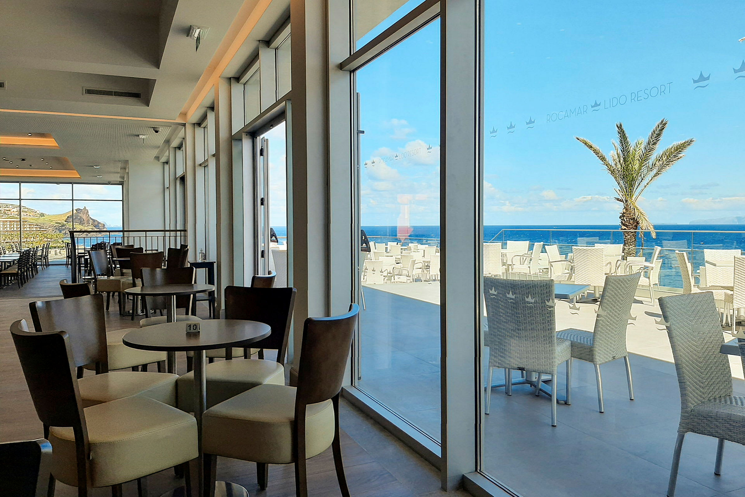 Bild av en restaurang med sittplatser inomhus och terrass med havsutsikt. (AI-genererad text)