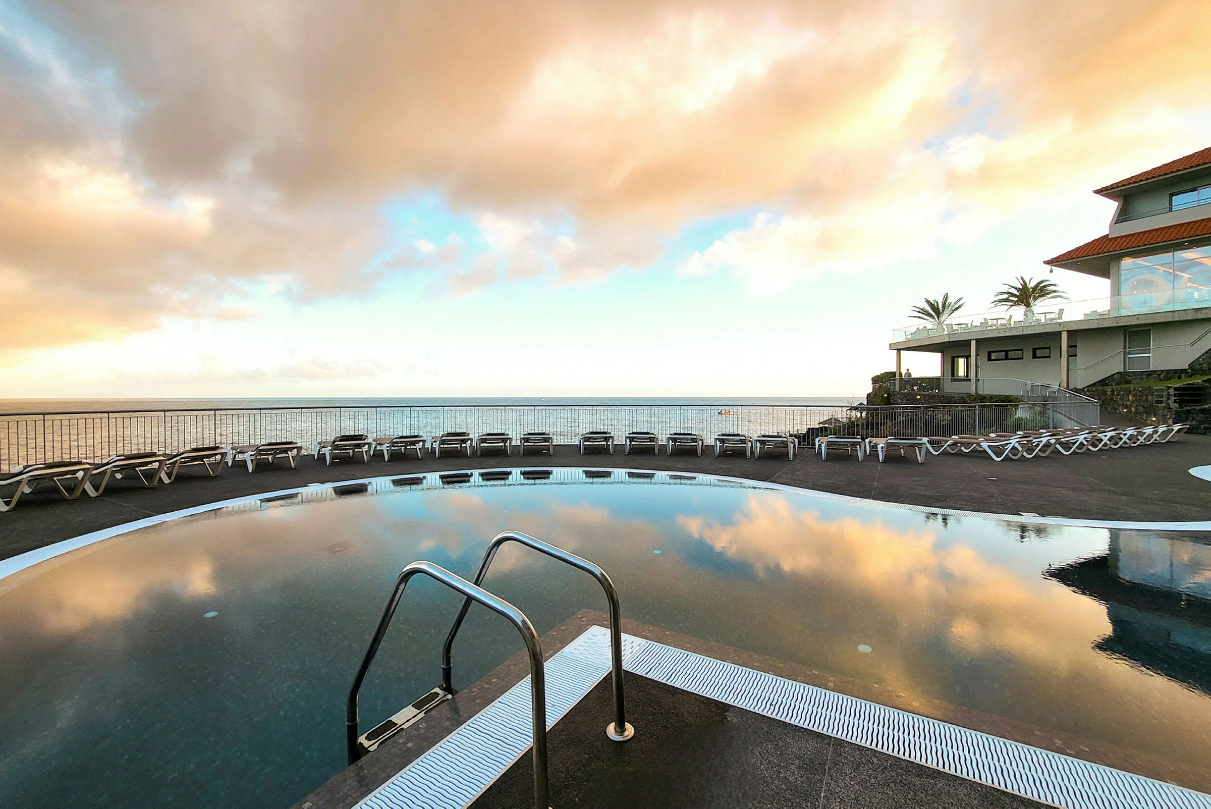 En utomhuspool med utsikt över havet och omgivande solstolar vid ett hotell. (AI-genererad text)
