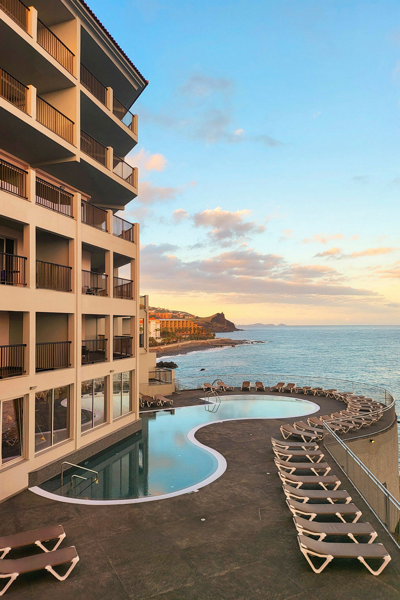 Ett hotell med en pool och solstolar vid havet under en klar himmel. (AI-genererad text)