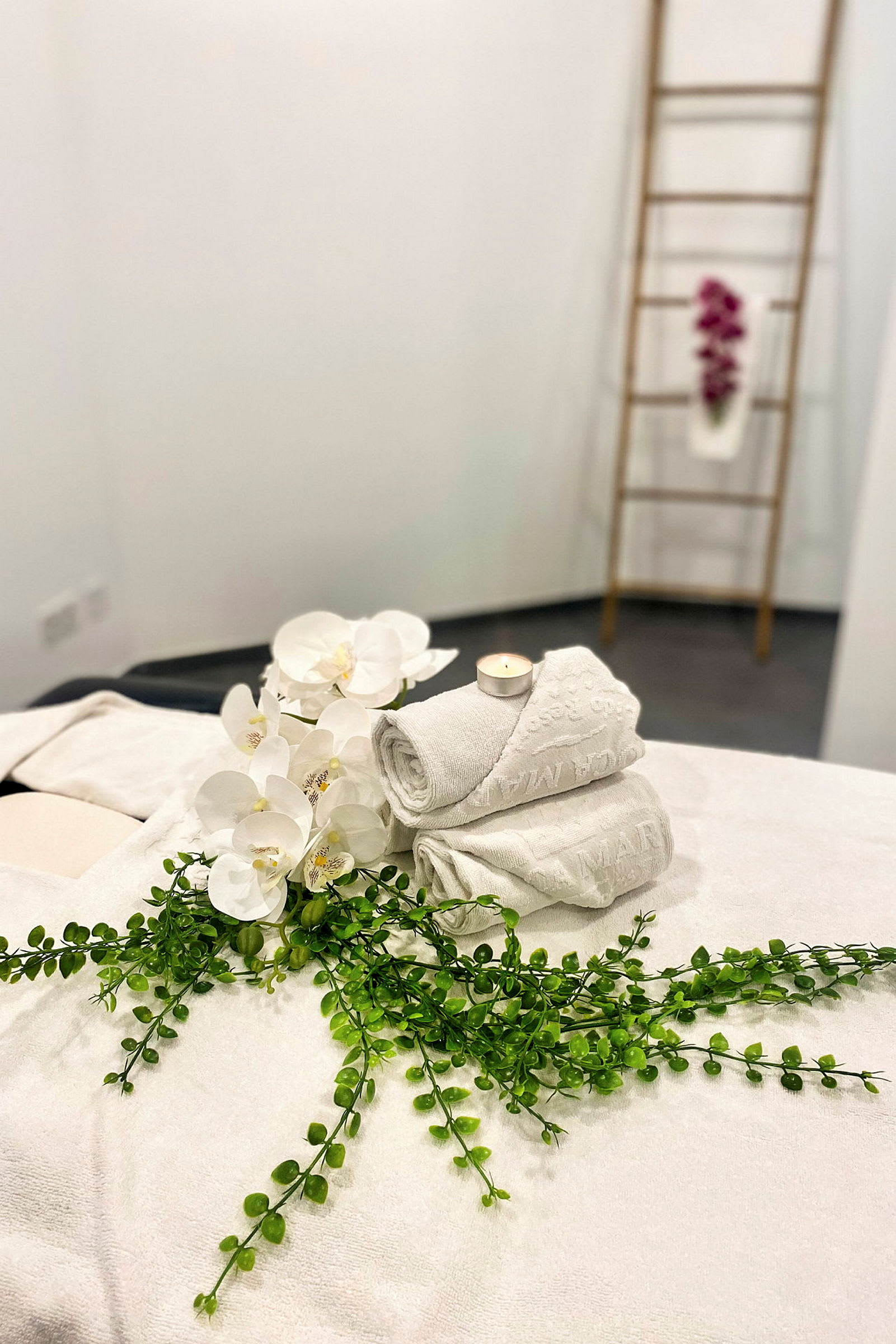 Vita handdukar, en gren grönska och vita orkidéer på en massagebänk i ett spa. (AI-genererad text)