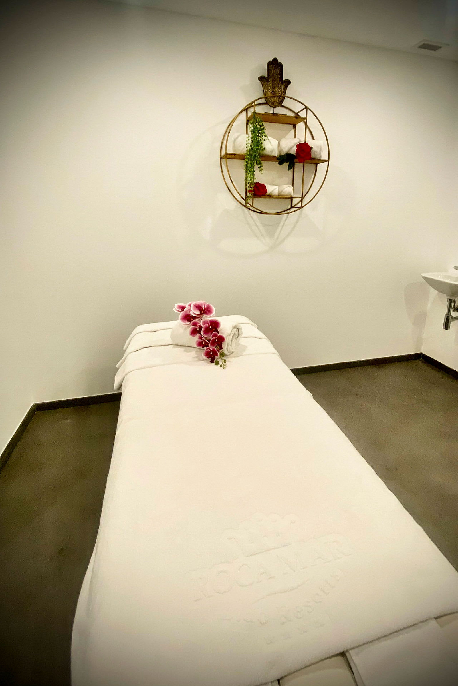 En massagebänk i ett spa-rum med handdukar och blommor. (AI-genererad text)