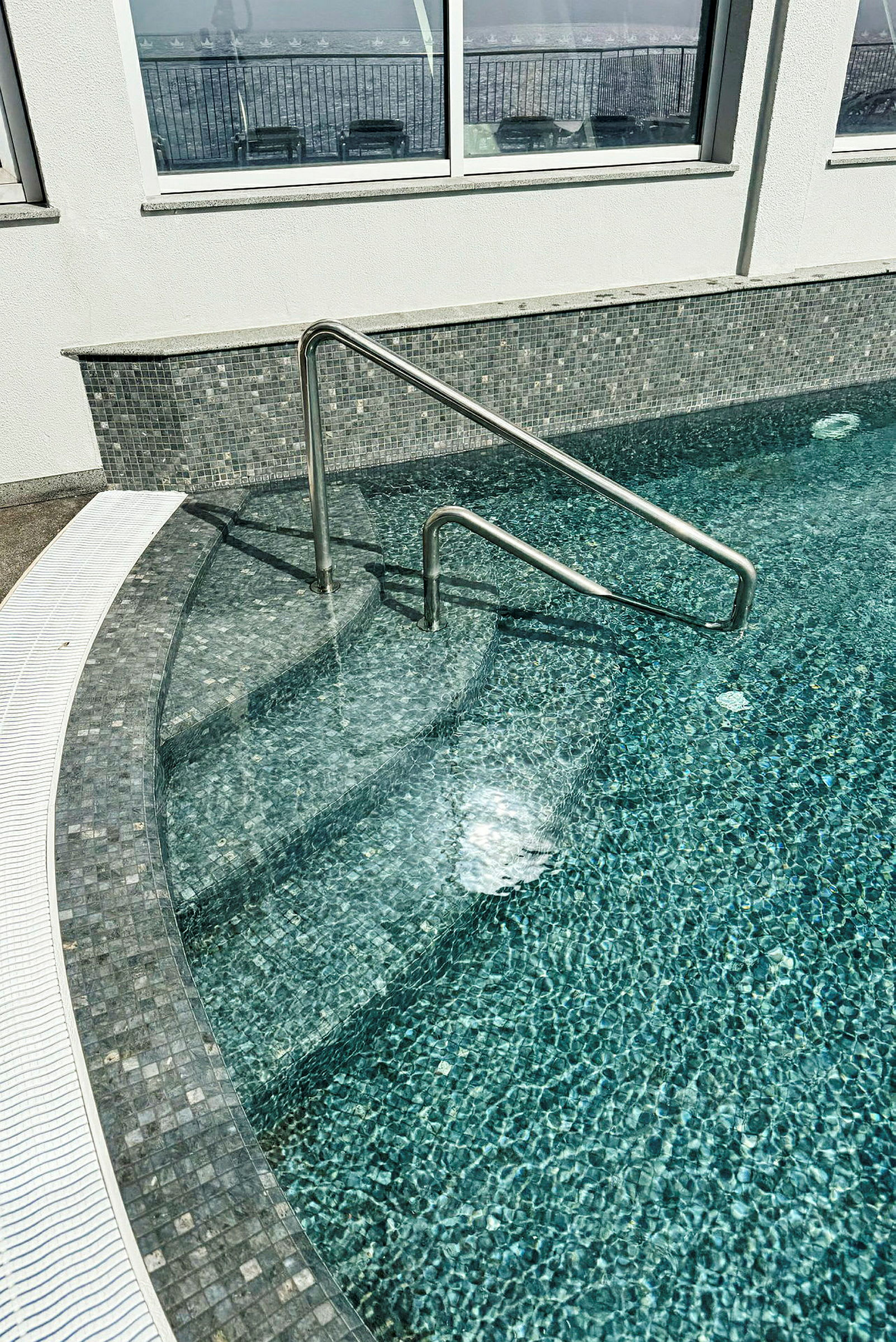 Inomhuspool med en metallräcke och klart vatten. (AI-genererad text)