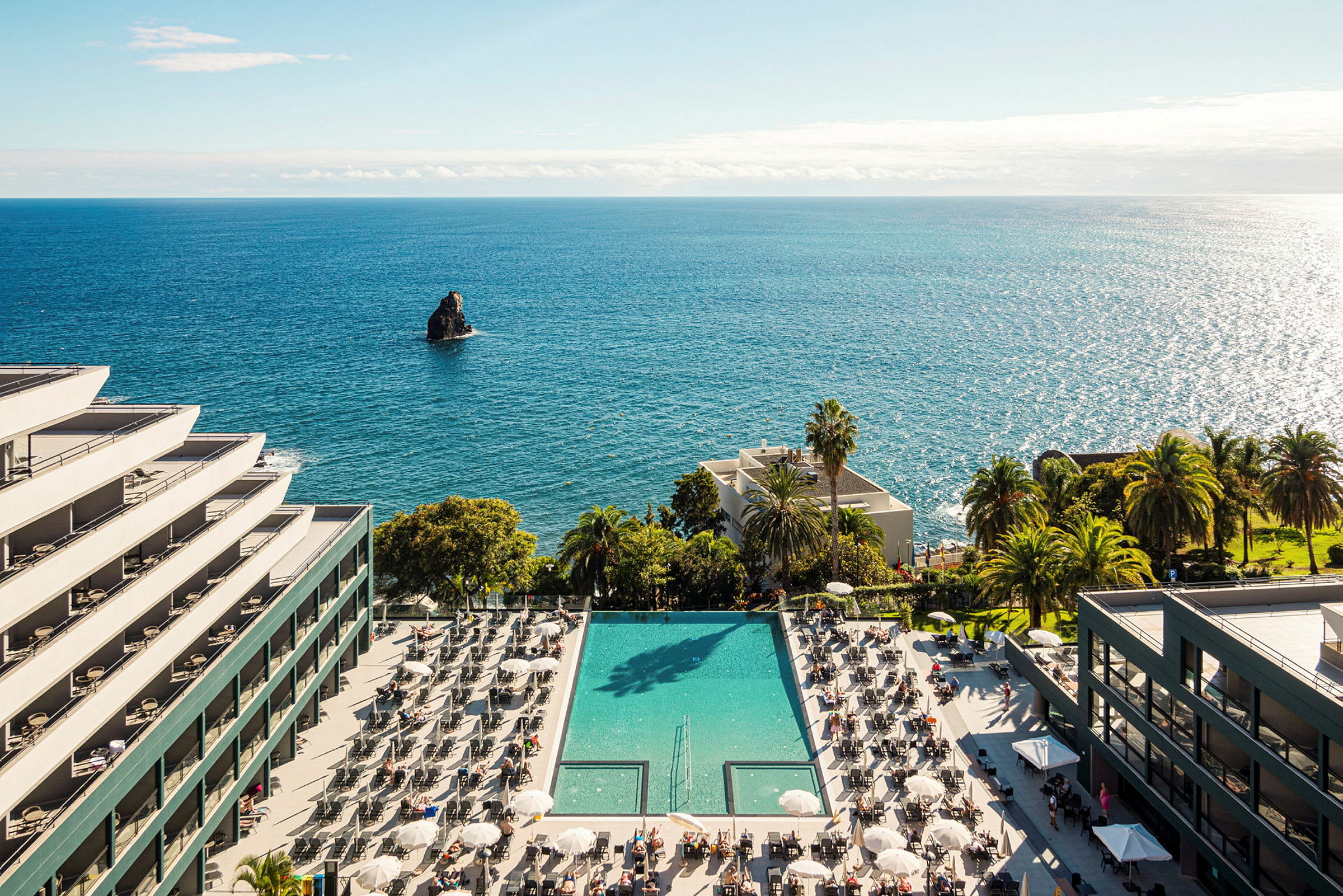 Hotell byggt vid havet med en pool och solstolar. (AI-genererad text)