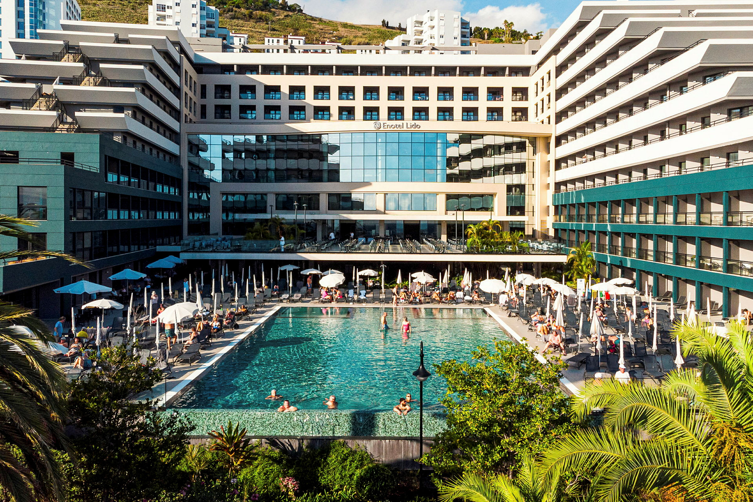 Hotellbyggnad med en stor utomhuspool och solstolar, omgiven av grönska. (AI-genererad text)