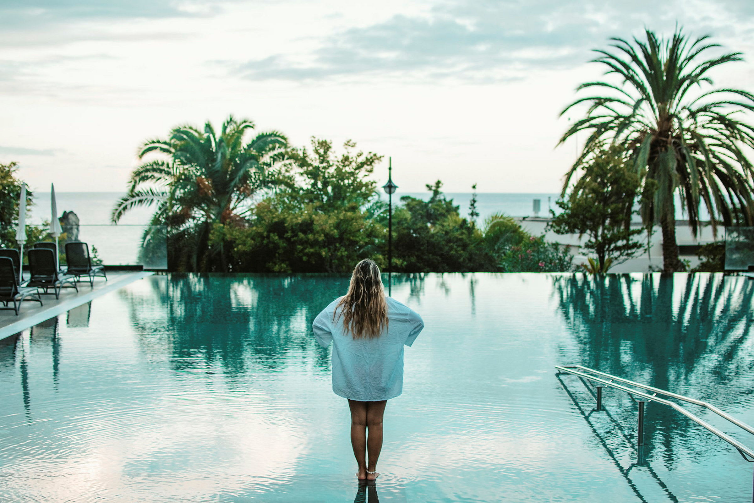 En person står vid kanten av en pool och tittar ut över träd och himmel. (AI-genererad text)