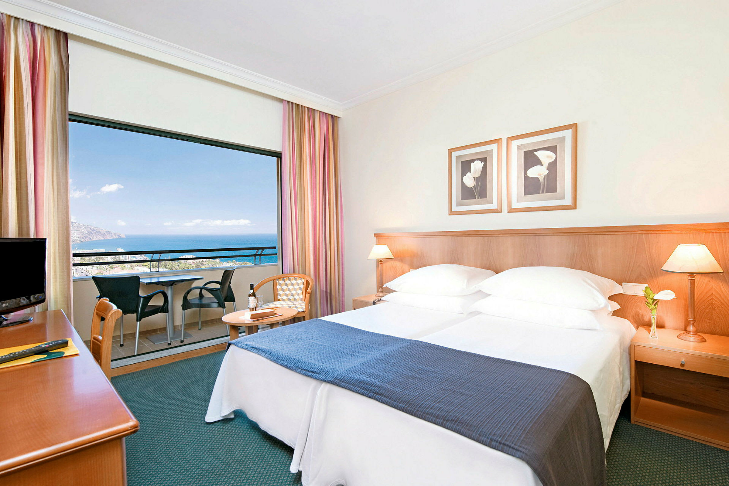 Hotellrum med dubbelsäng, nattduksbord och balkong med utsikt över havet. (AI-genererad text)