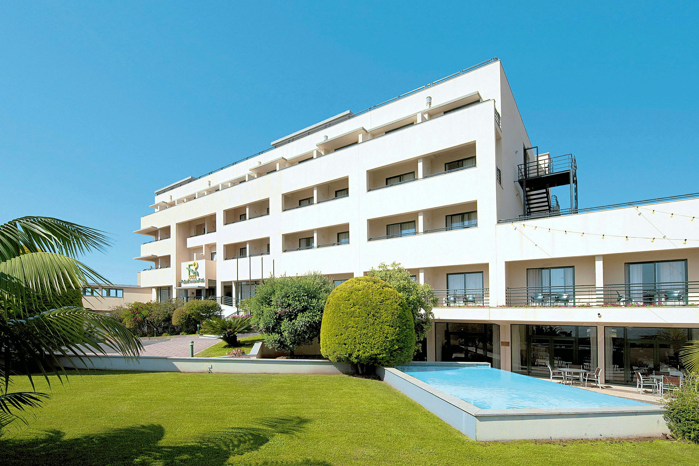 Bild av ett hotell med vita fasader, grönt gräs och en liten pool. (AI-genererad text)