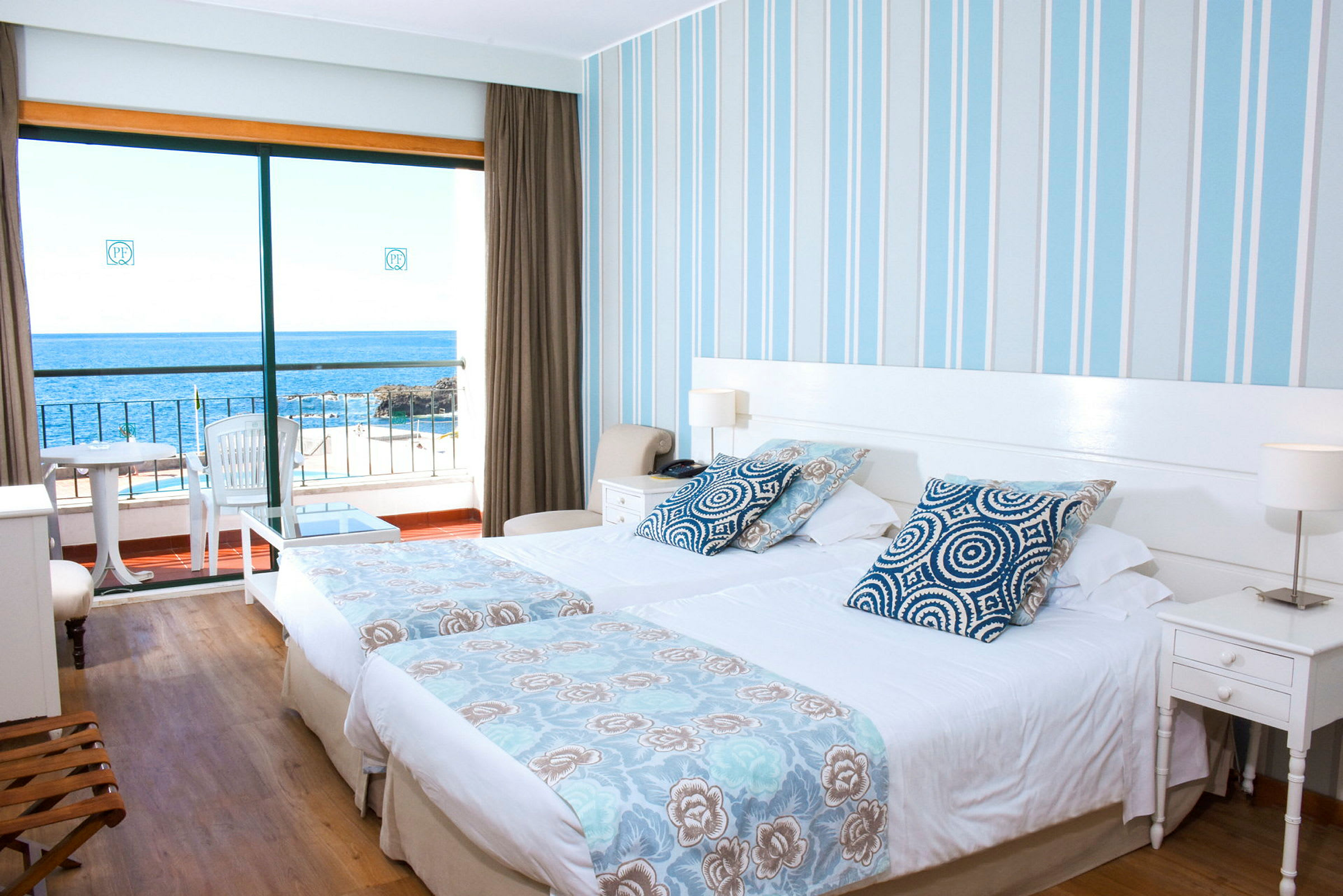 Hotelrum med två enkelsängar, blått och vitt tema i designen, och en balkong med utsikt över havet. (AI-genererad text)