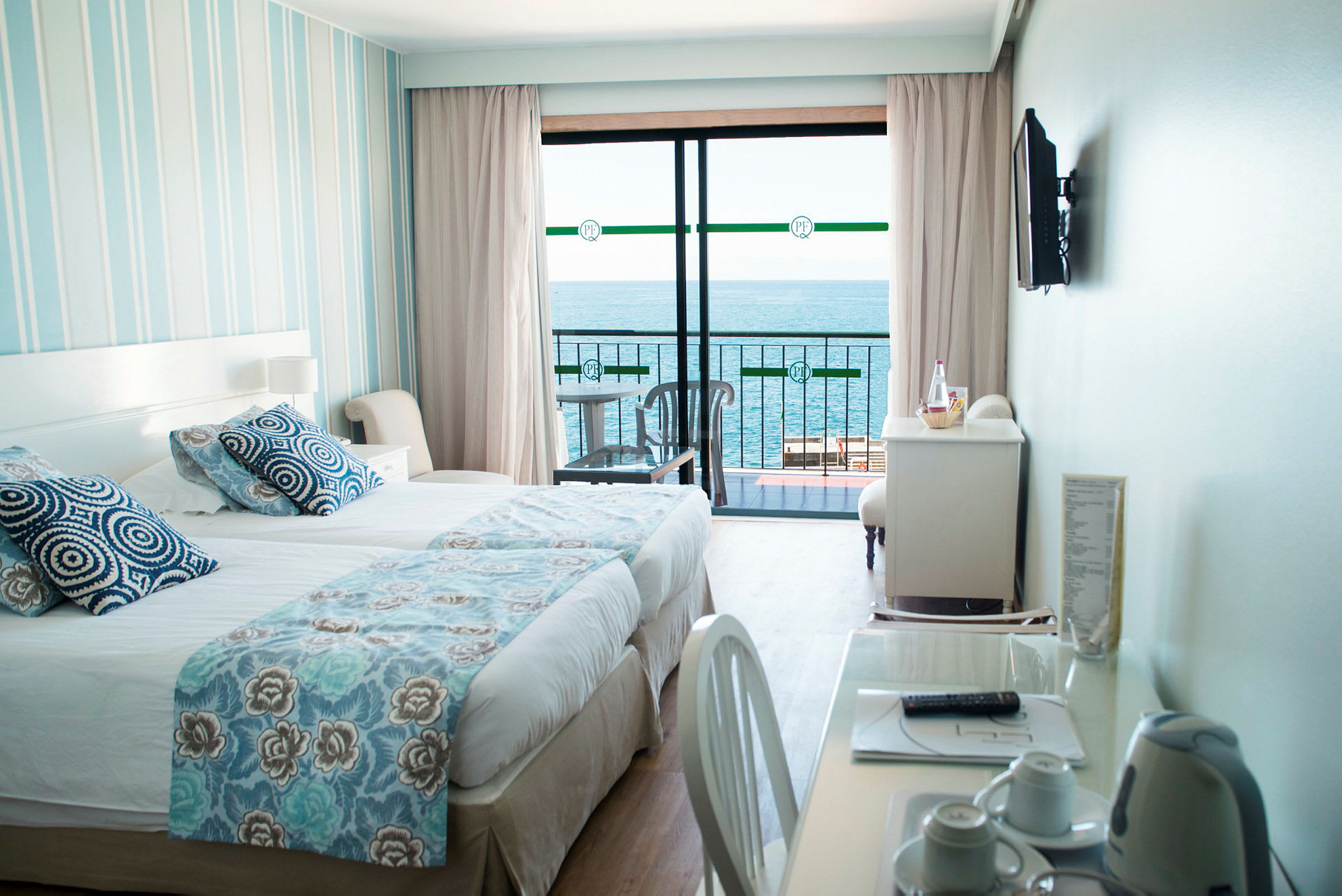 Ett hotellrum med en säng, ett skrivbord och utsikt över havet från en balkong. (AI-genererad text)