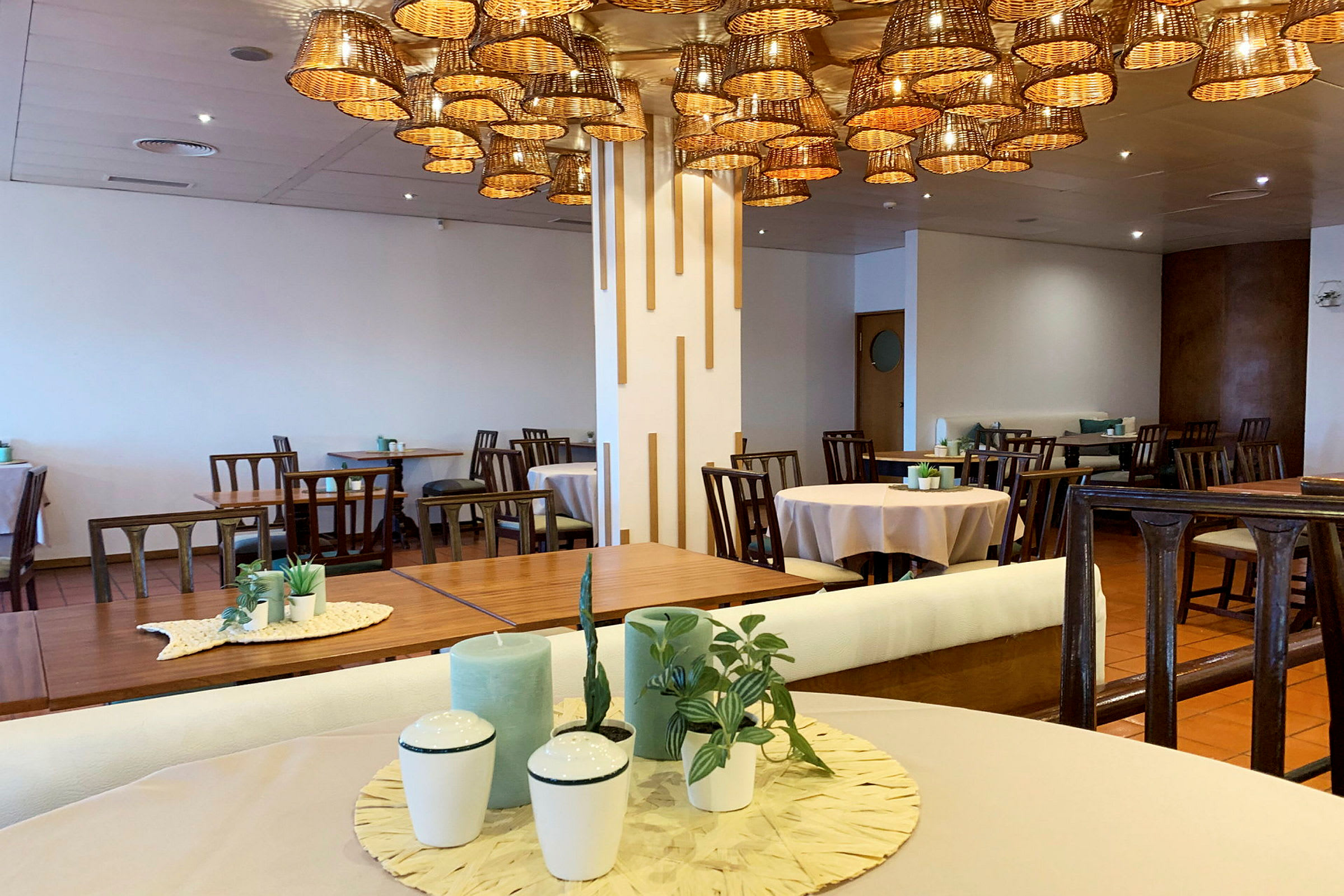 Ett rum inrett som en restaurang, med bord, stolar och en ljuskrona av korgar. (AI-genererad text)