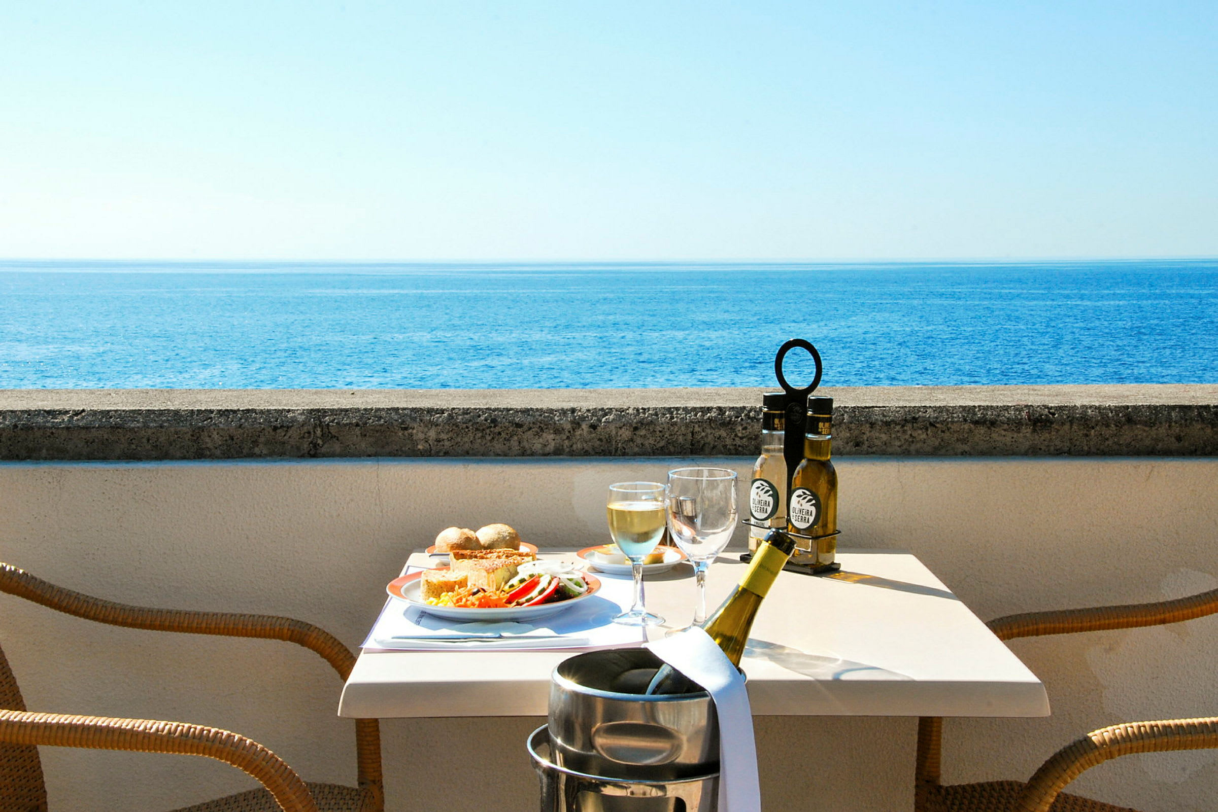 Utsikt över havet från en terrass med ett dukat bord som har mat och dryck. (AI-genererad text)
