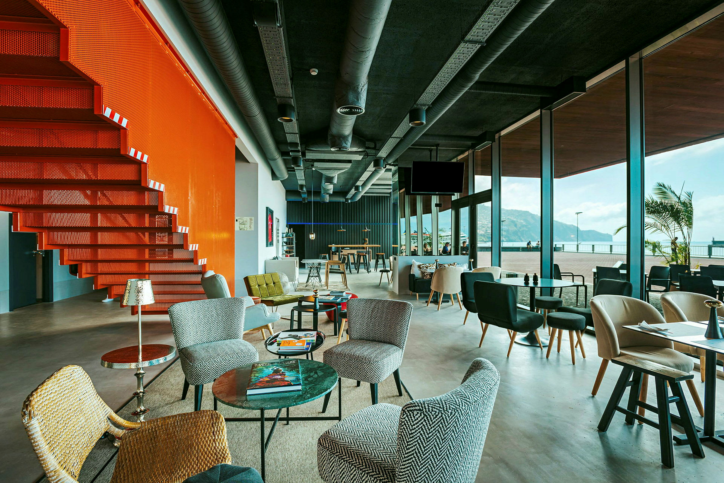 En modern lounge med stora glasfönster och en orange trappa. (AI-genererad text)
