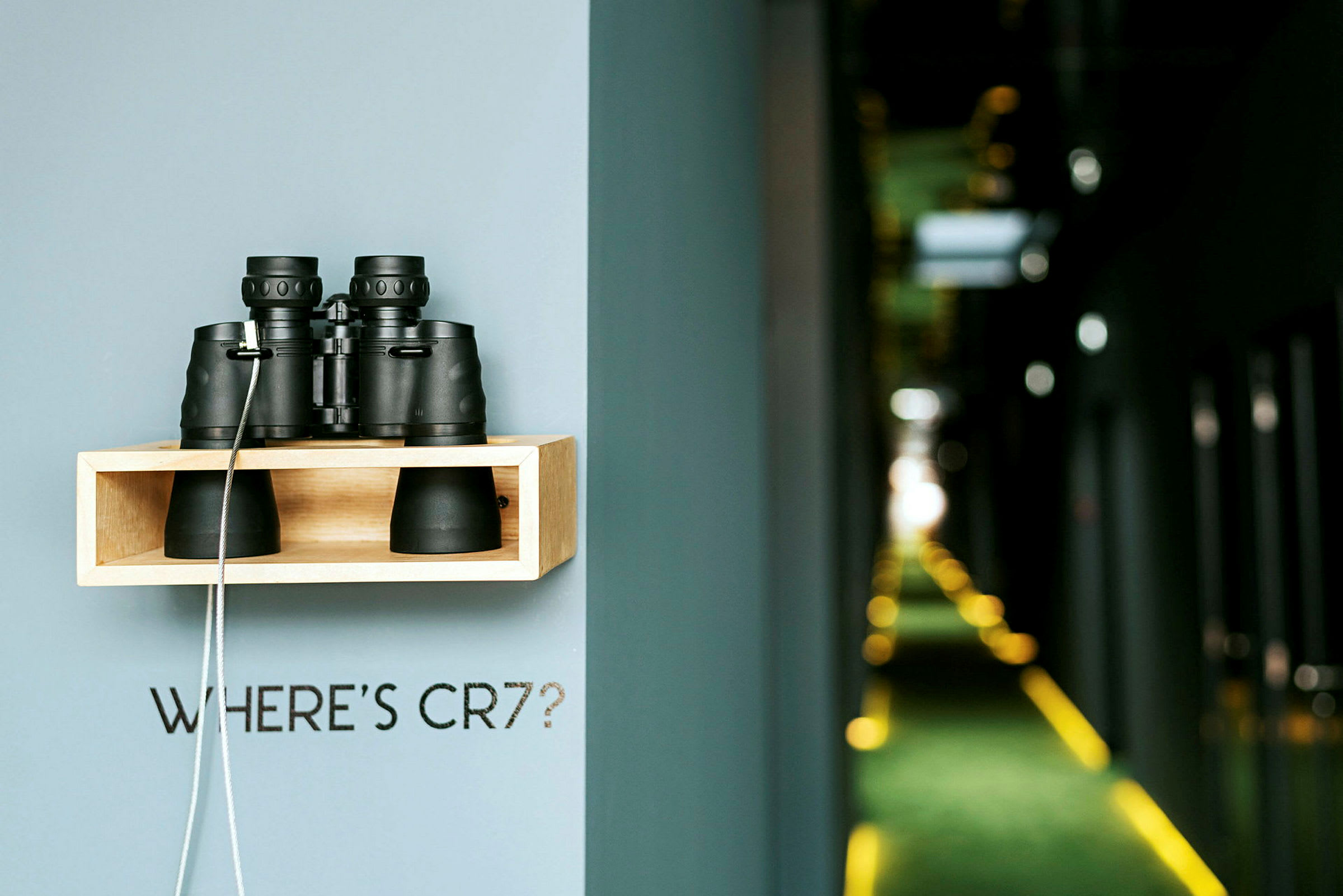 En hylla monterad på en vägg med en kikare placerad ovanpå och en text som lyder "WHERE'S CR7?", med en oskarp korridor i bakgrunden. (AI-genererad text)