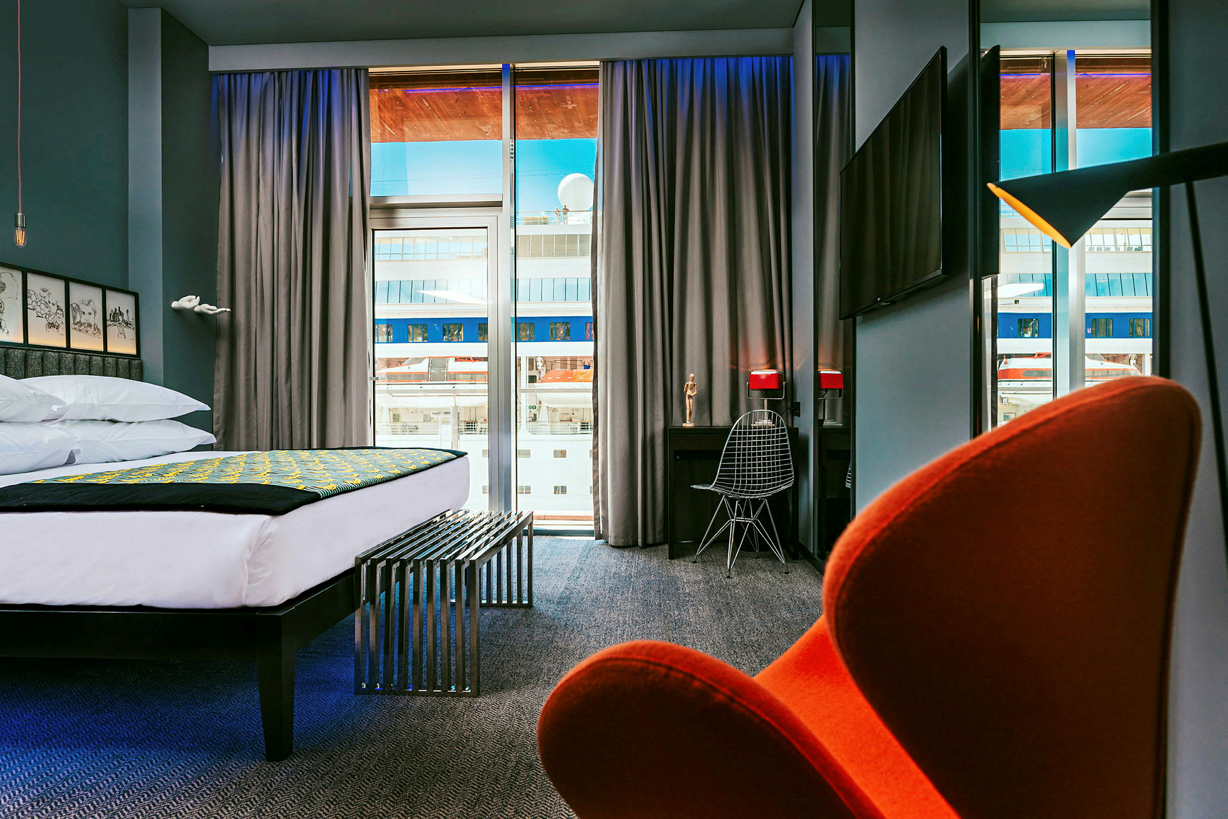 Modernt hotellrum med stor säng, skrivbord och stol samt utsikt genom stora fönster. (AI-genererad text)