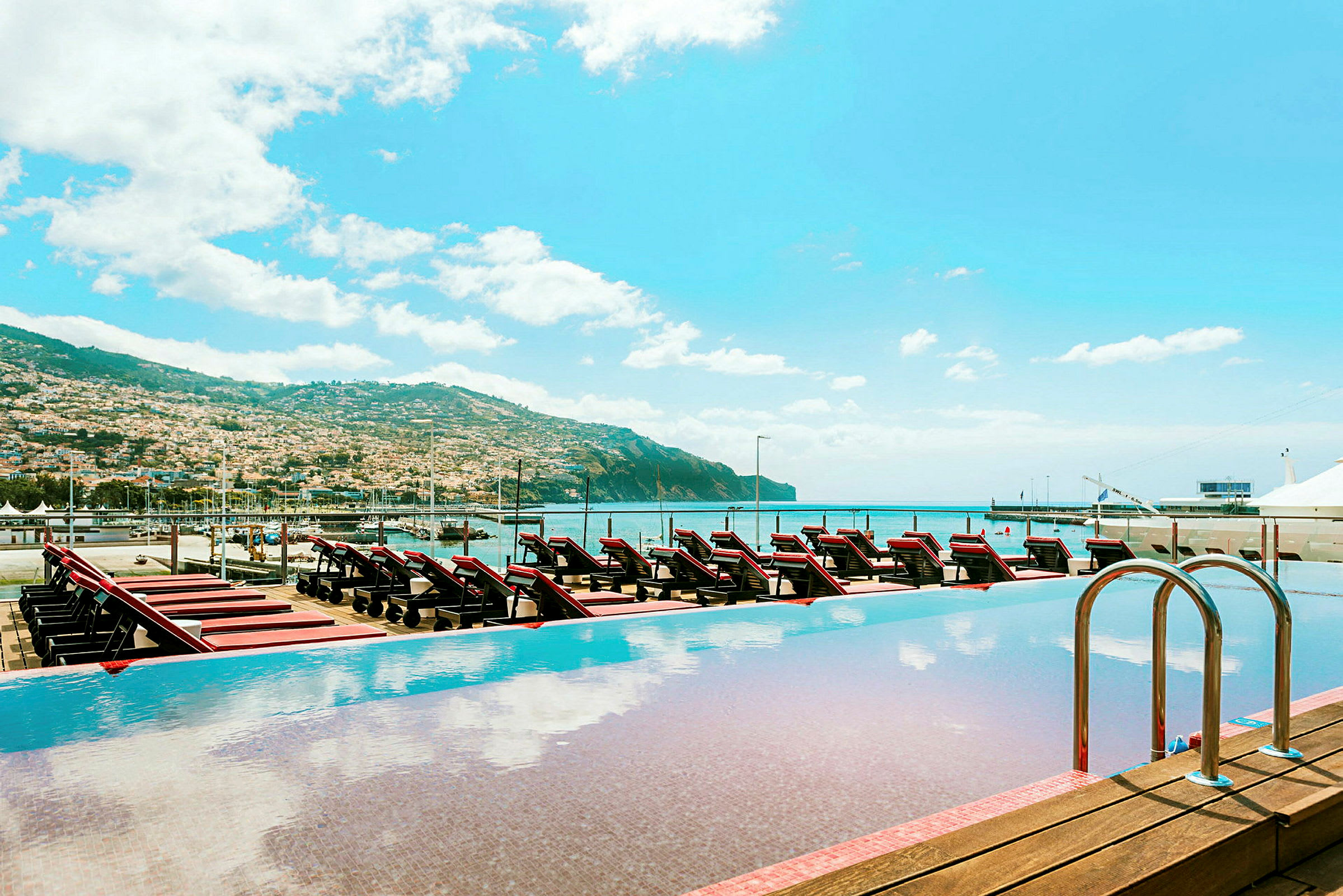 Infinitypool med utsikt över solstolar, havet, och en omgivande bergslandskap. (AI-genererad text)