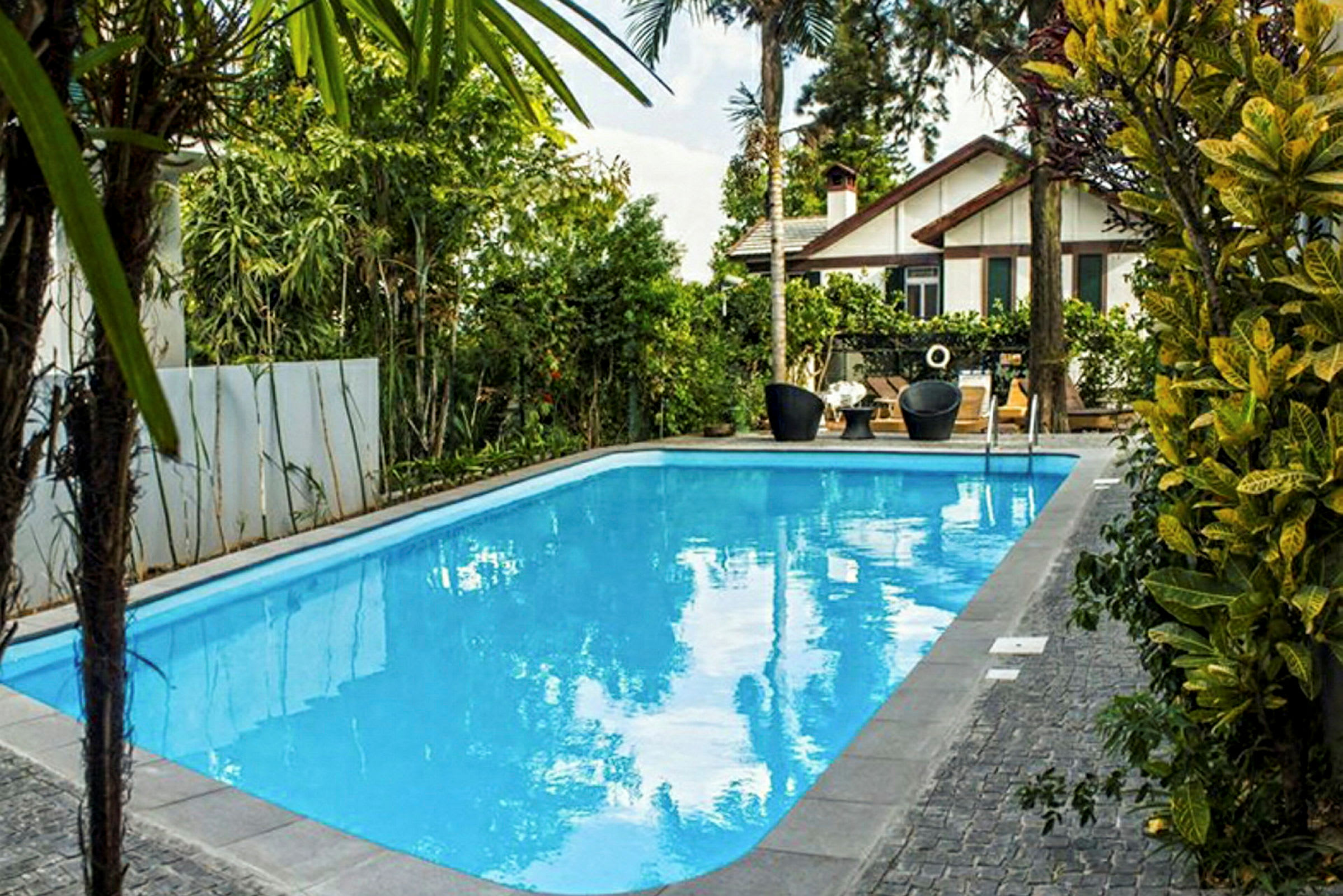 Utomhuspool omgiven av grönska med en villa i bakgrunden. (AI-genererad text)