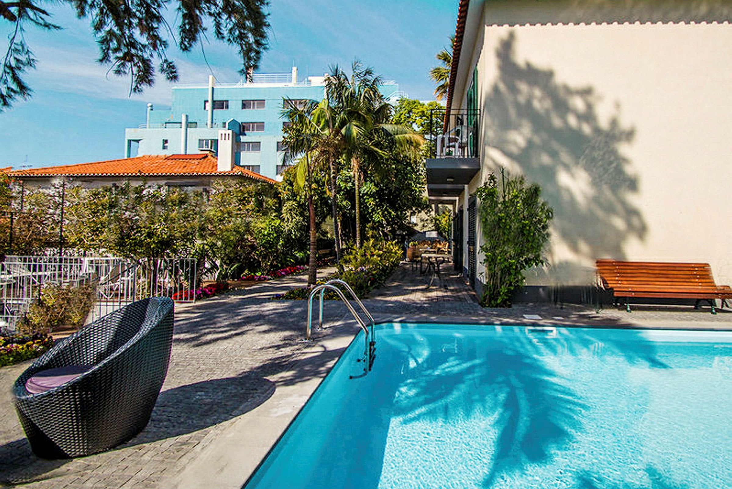 Bild av en pool med sittmöbler och omgivande trädgård samt byggnader i bakgrunden. (AI-genererad text)