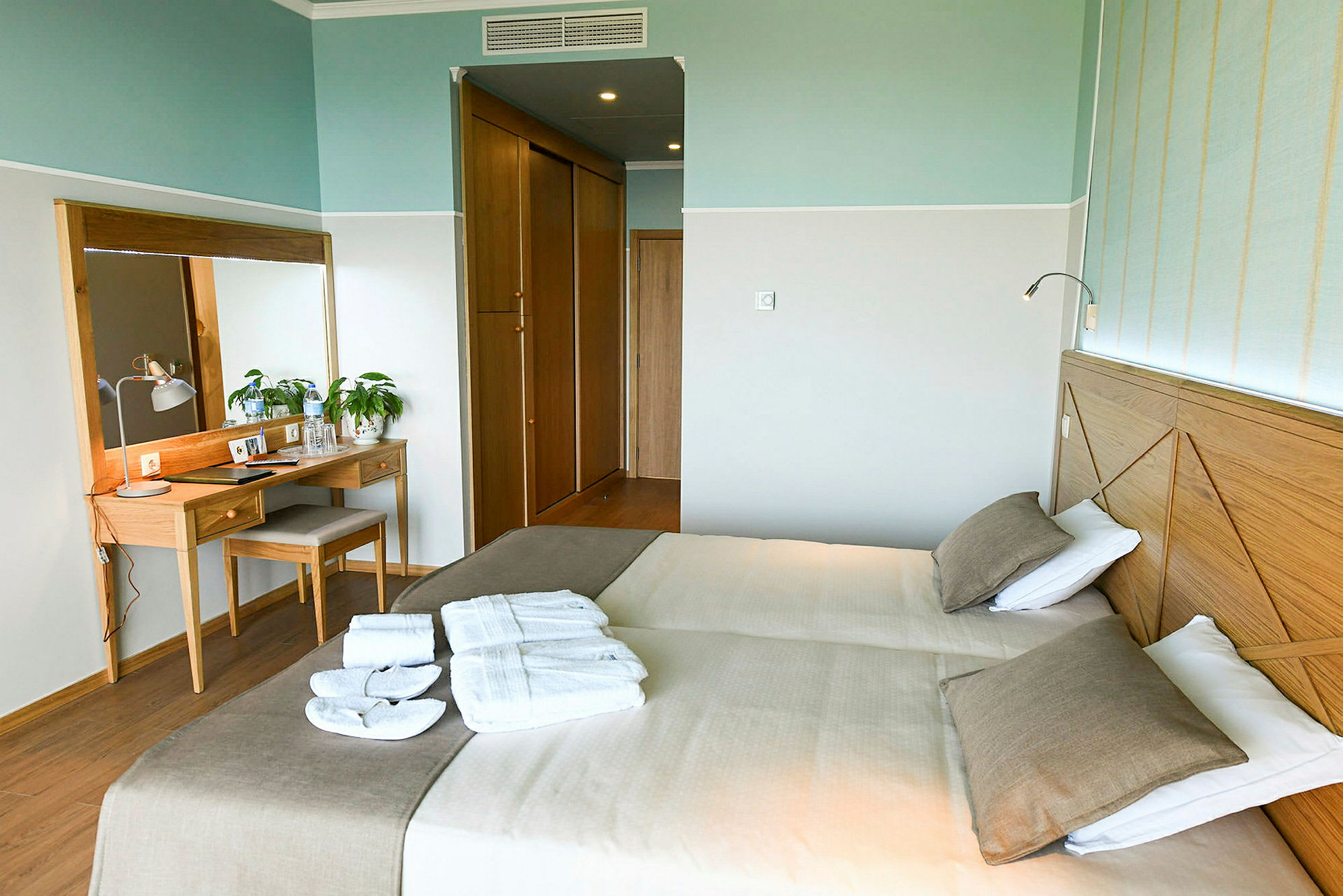Hotellrum med två enkelsängar, en spegel och ett skrivbord. (AI-genererad text)