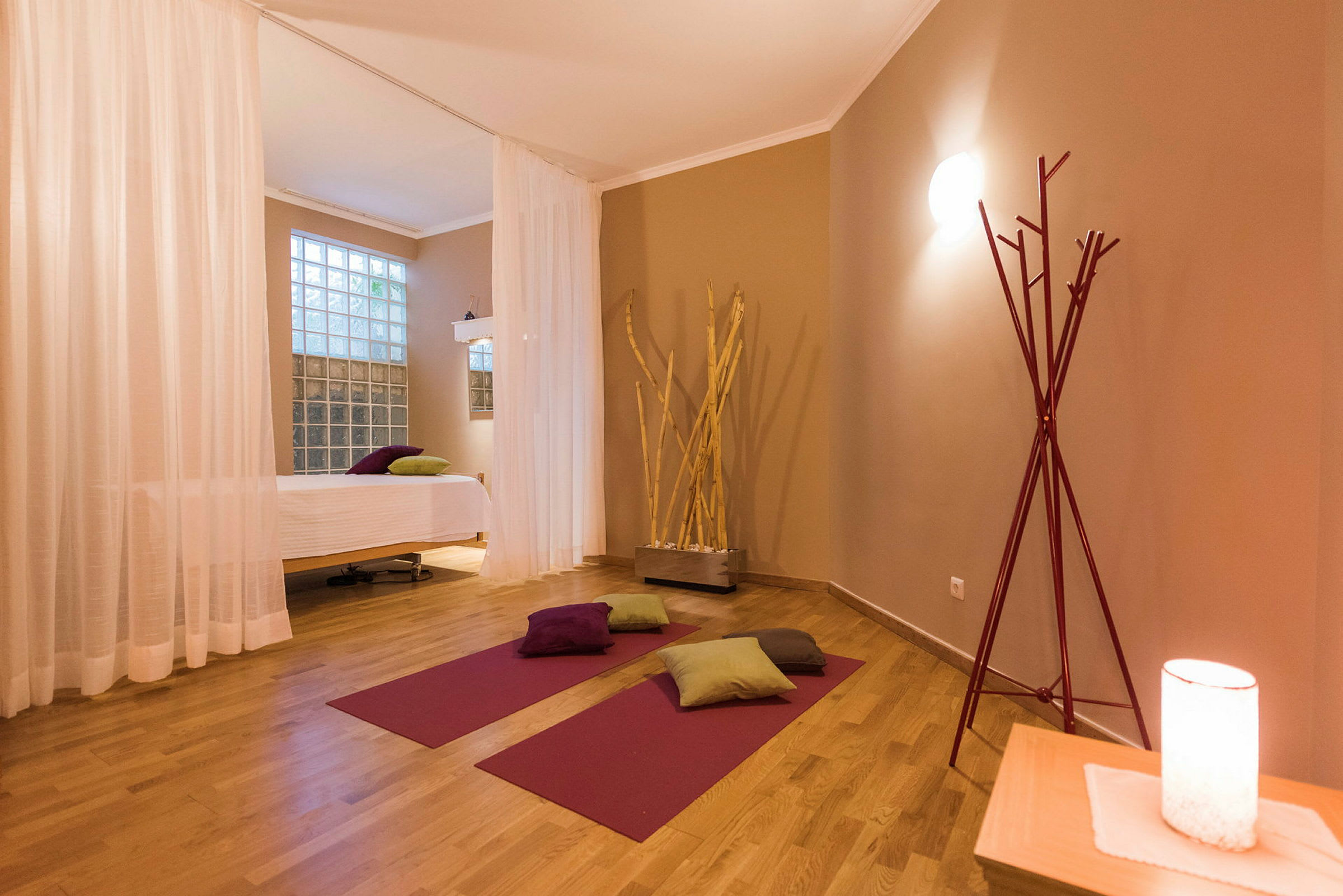 Ett yogarum med mattor, kuddar och en massagebänk, inrett med varma färgtoner. (AI-genererad text)