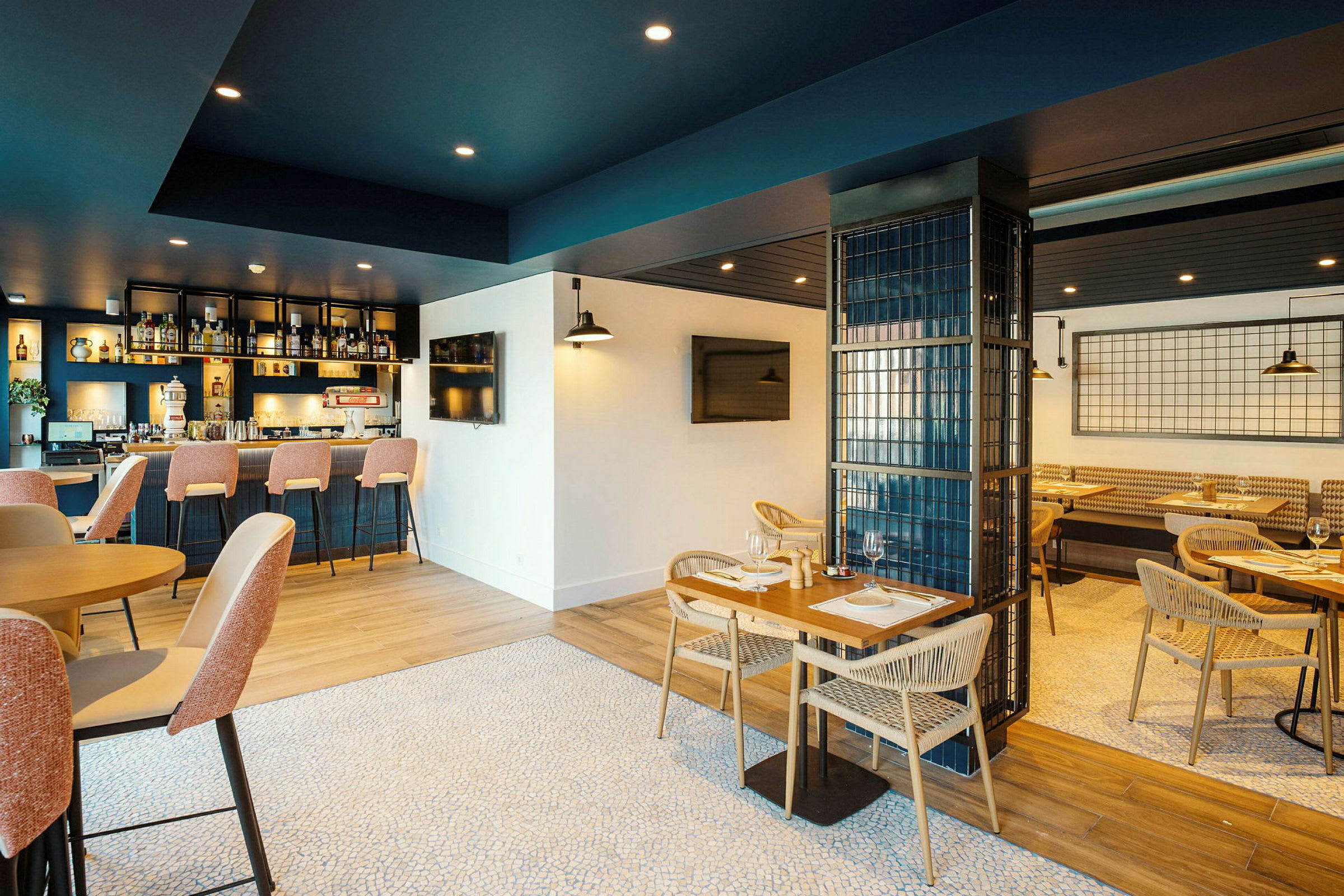 En restaurang med modern inredning. Det finns en bardisk med sittplatser och bord med stolar för matservering. (AI-genererad text)