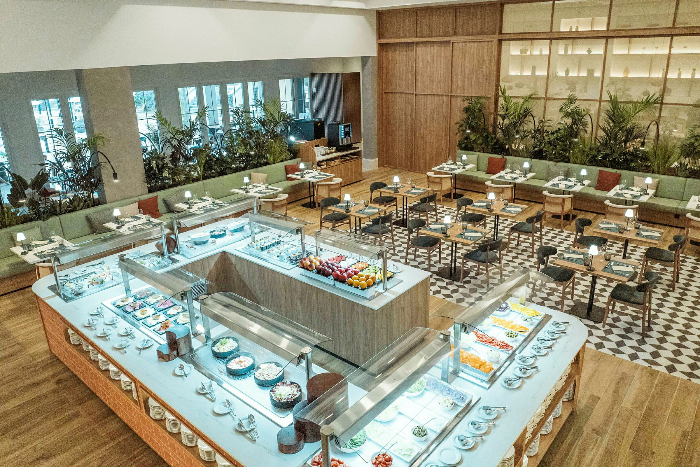 Ett väl upplyst restaurangområde med buffébord i förgrunden fyllt med olika maträtter samt sittplatser i bakgrunden. (AI-genererad text)