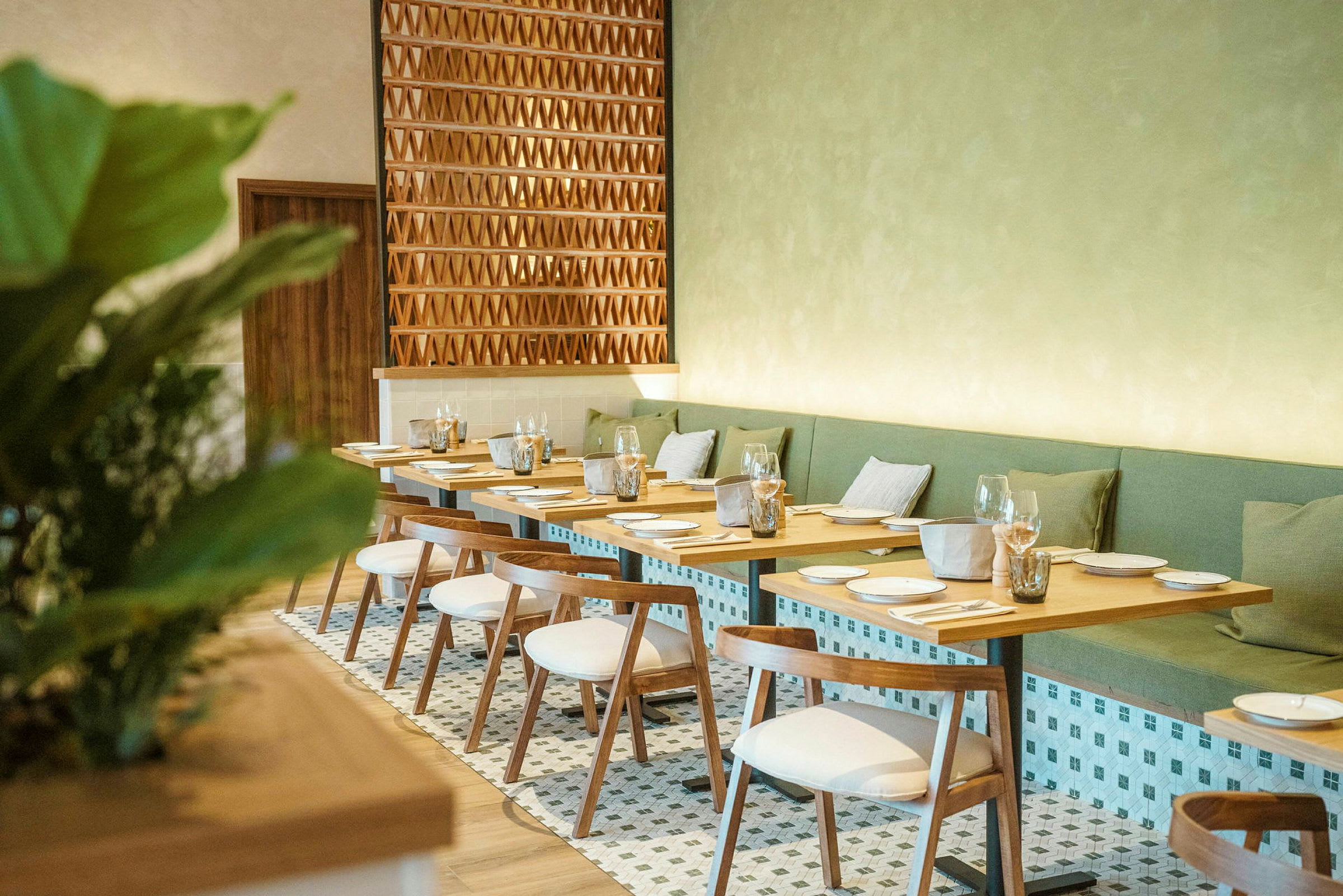 En elegant restaurang med träbord och vita stolar samt gröna sittkuddar mot väggen. (AI-genererad text)