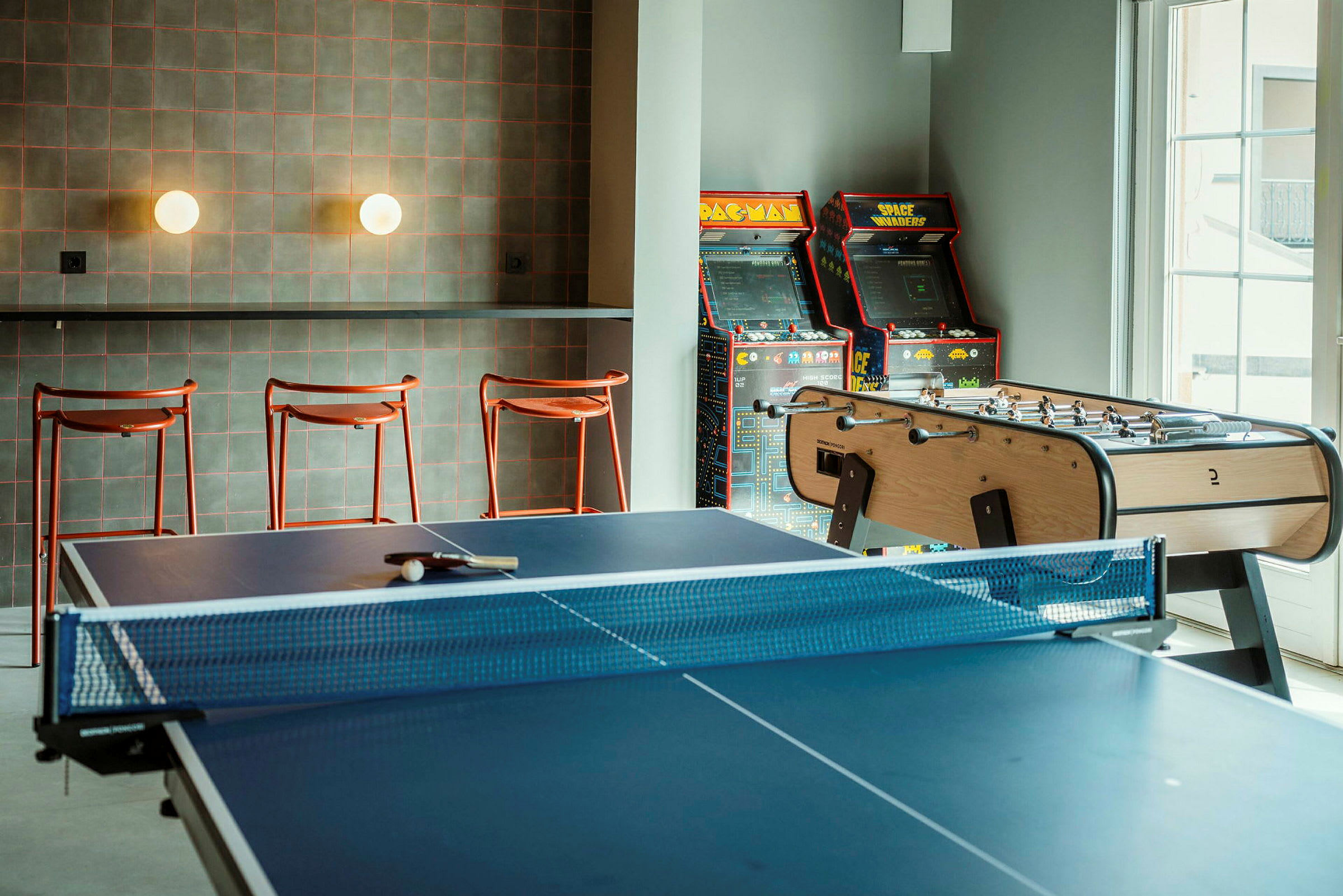 Ett rum med ett bordtennisbord, ett fotbollsspel och arkadmaskiner vid väggen. (AI-genererad text)