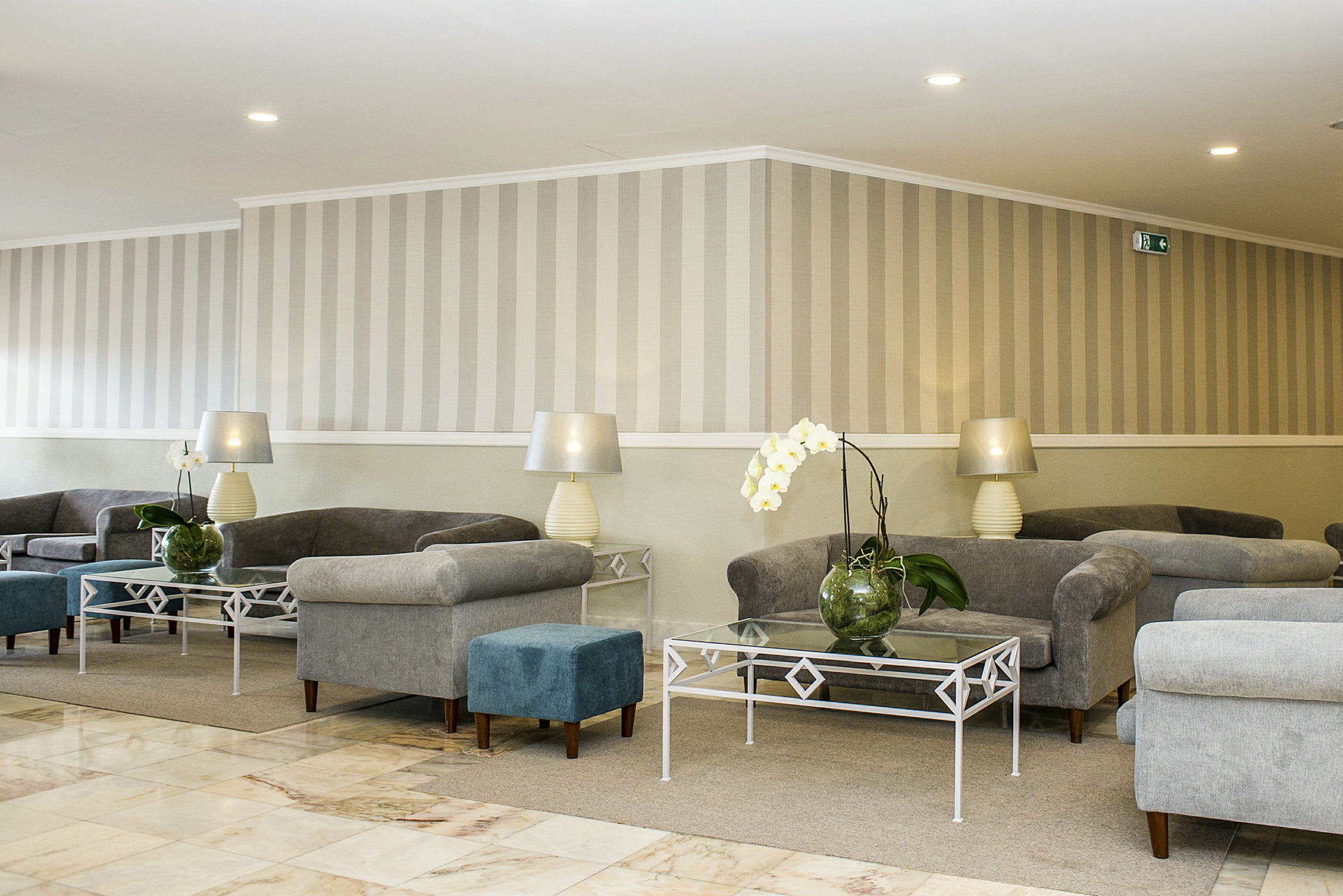 En inomhus lounge med gråa fåtöljer, glasbord och dekorativa blommor. (AI-genererad text)
