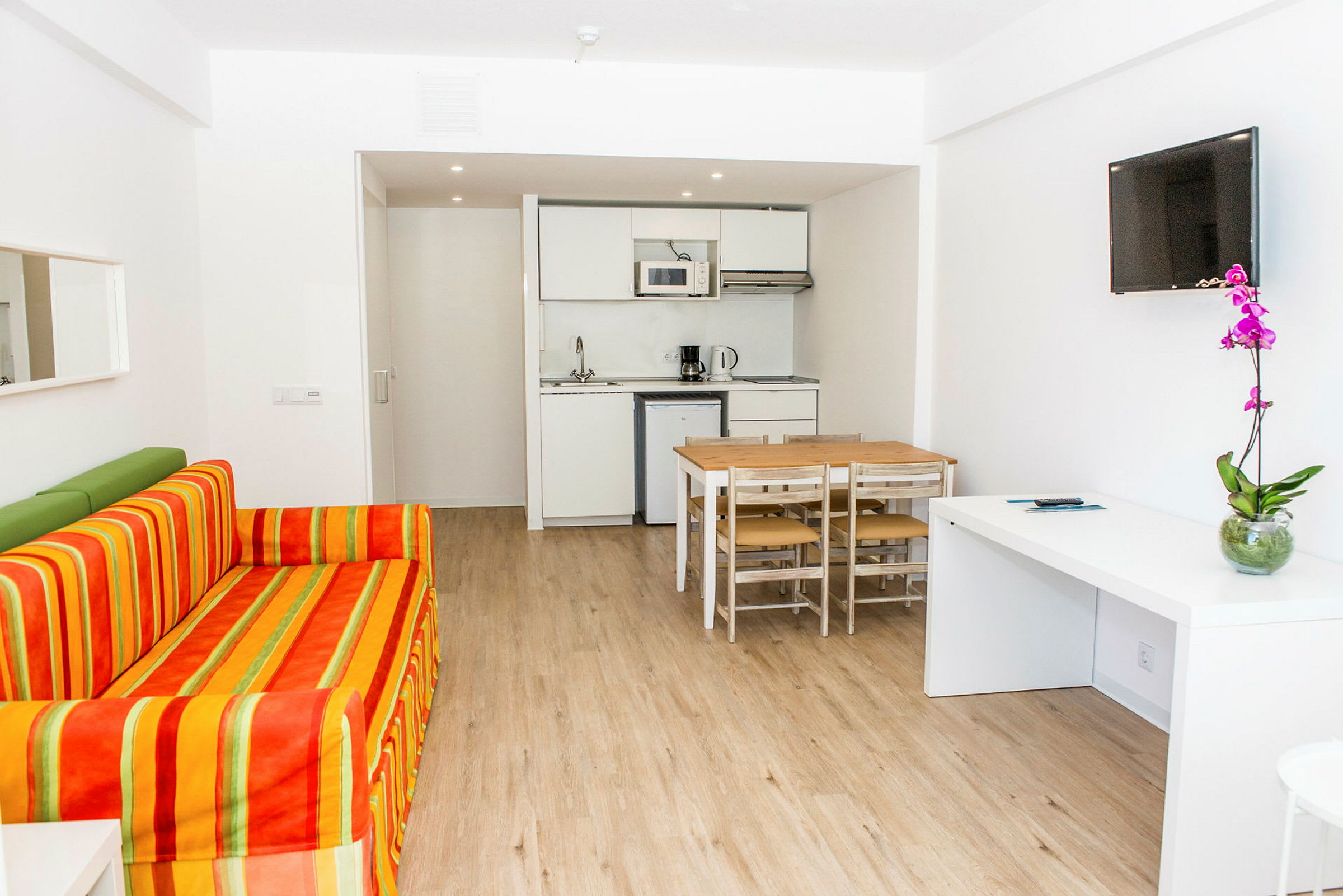 Bild av ett modernt hotellrum med soffa, matbord, köksavdelning och TV. (AI-genererad text)