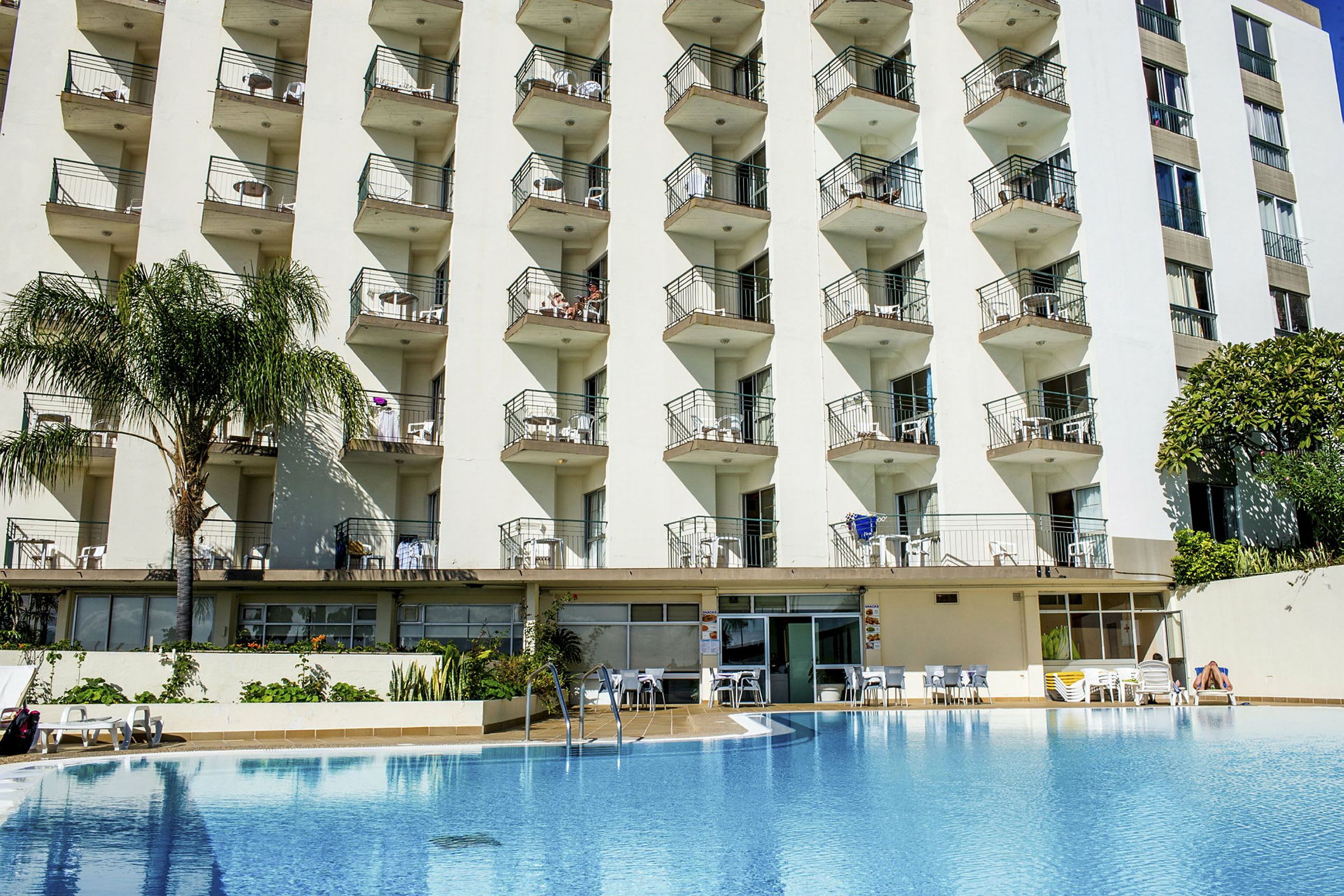 Hotellfasad med flera balkonger över en pool. (AI-genererad text)