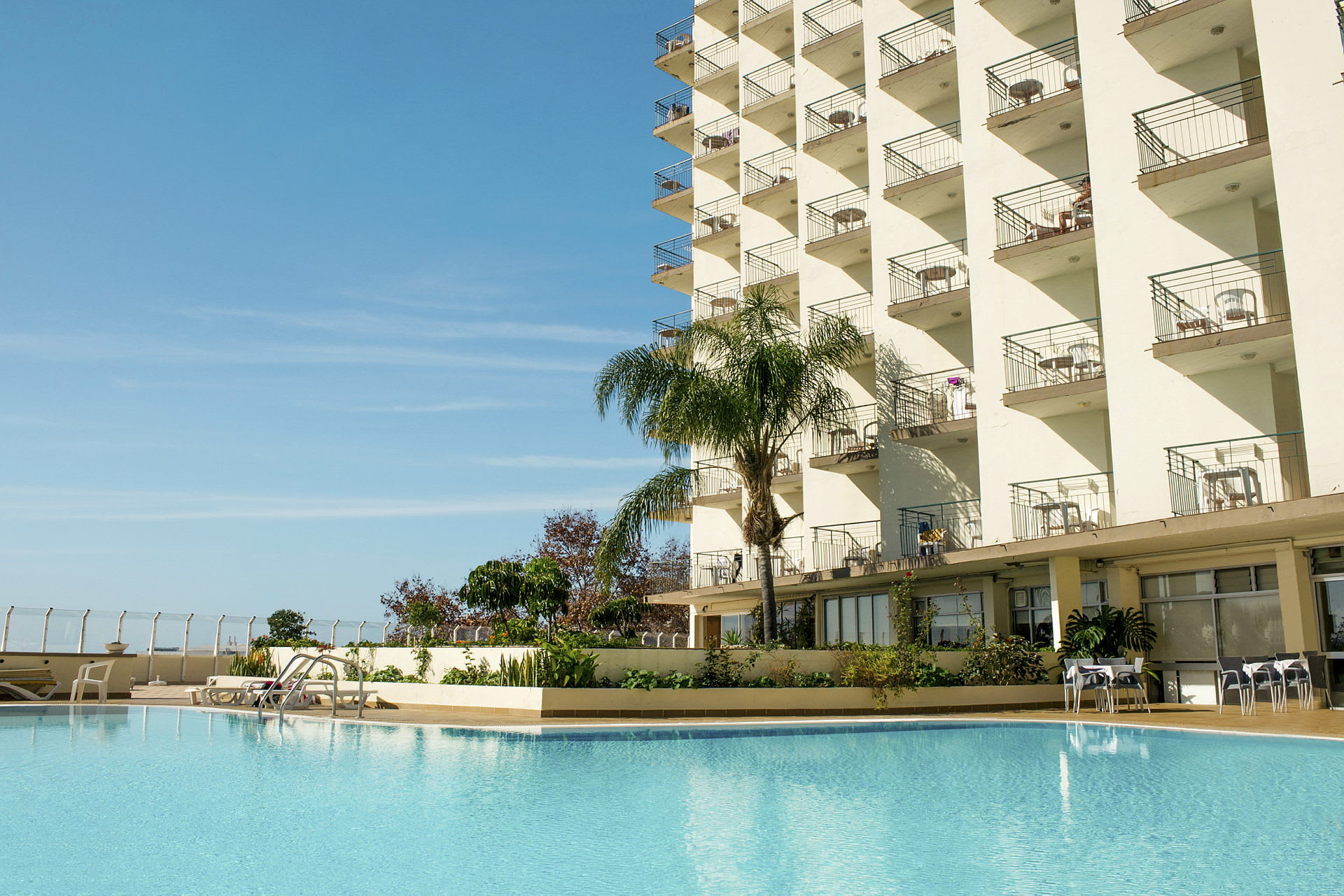 Hotellbyggnad med balkonger och en pool framför. (AI-genererad text)